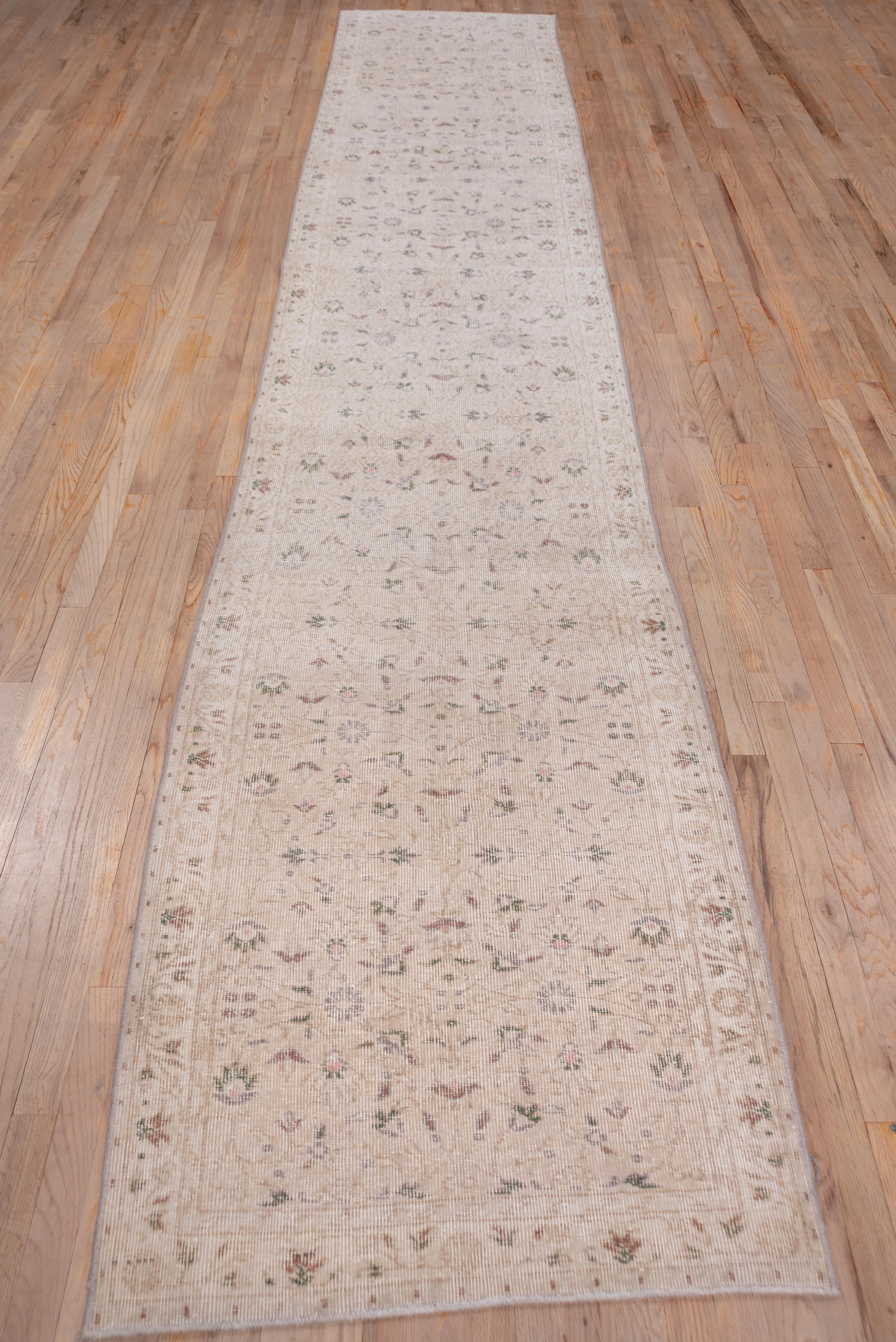 This solidly woven runner shows a sandy ecru field with arabesques and small rosettes and palmettes in an allover, repeating pattern. The tonally en suite border shows a budding tendril, rosettes and simple palmettes.