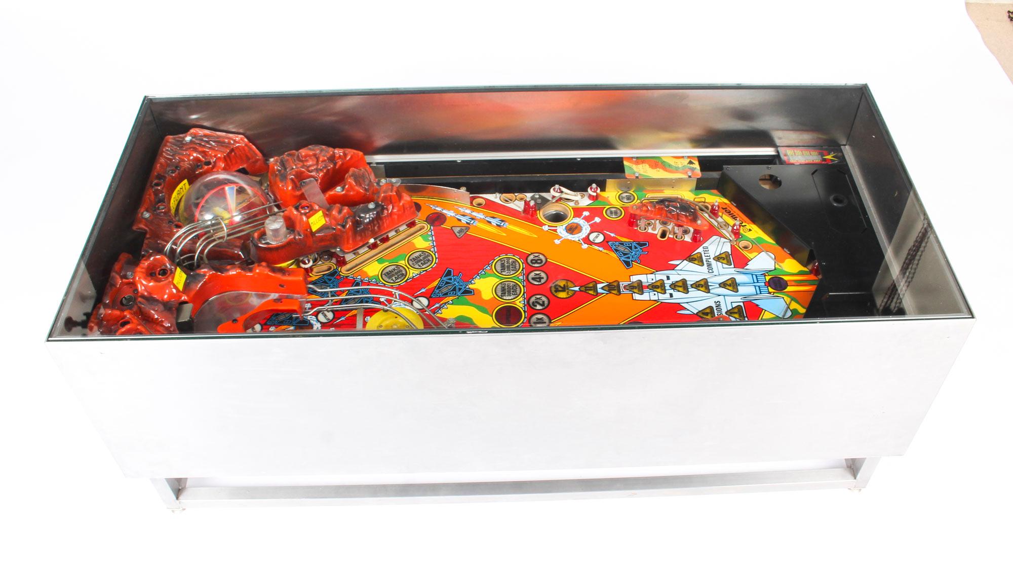 This is an original Gottlieb pinball machine that was cleverly converted into a coffee table, the pinball components are circa 1960 in age.

The colourful coffee table is rectangular in shape and made of stylish brushed steel with a glass top. 
