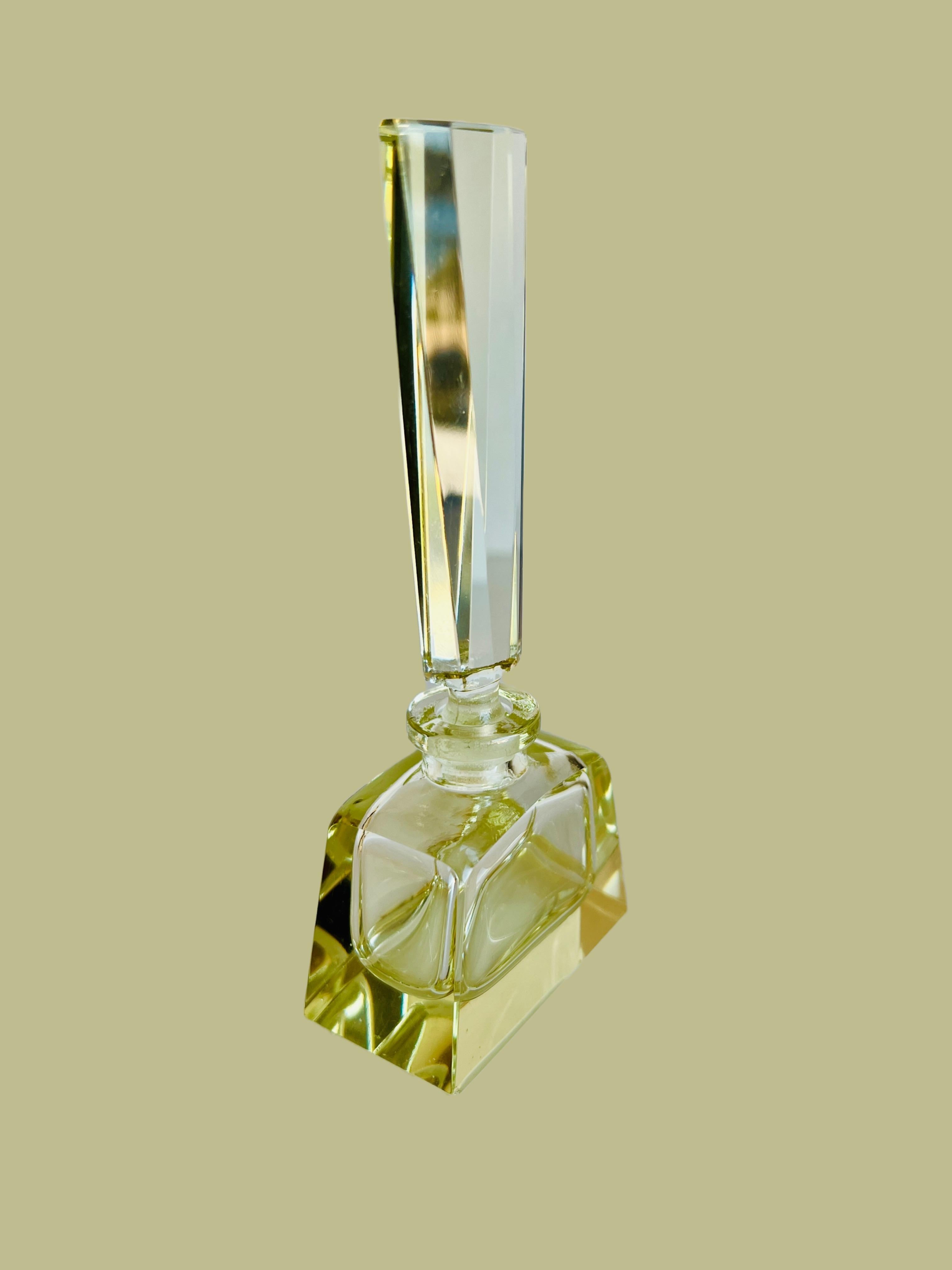 Dieser schöne Parfümflakon verkörpert die Anmut und Raffinesse einer vergangenen Epoche. Der Flakon aus hochwertigem Kristall mit einem zarten, hellgelben Farbton hat einen kühnen, rechteckigen Körper, der auf einem massiven, quadratischen Sockel