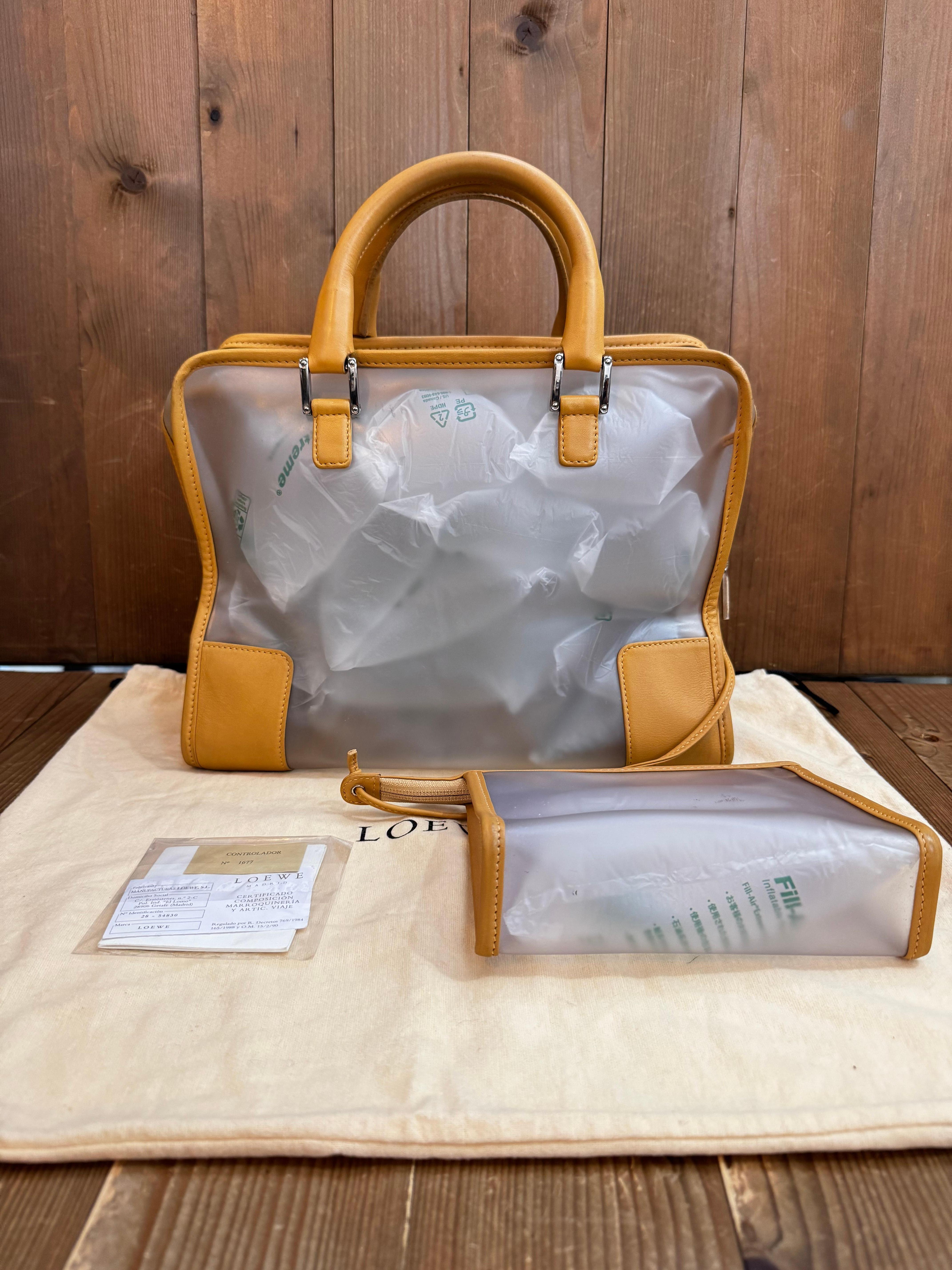 Ce sac boston Amazona vintage de LOEWE est confectionné en vinyle translucide et en cuir de veau marron, avec des ferrures argentées et des anses en cuir roulées. La fermeture à glissière sur le dessus ouvre sur un intérieur non doublé comprenant