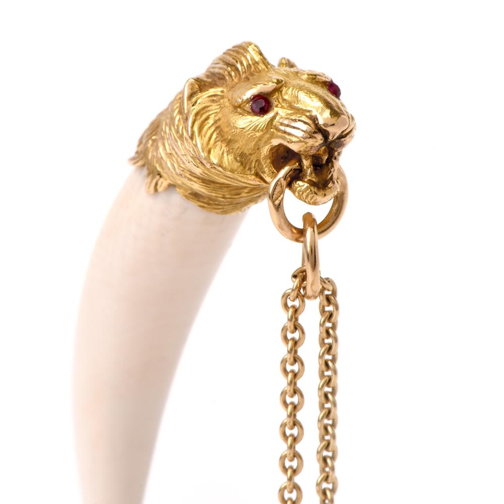 This enchanting and collectible lion head pendant of artistic workmanship is rendered in tooth bone and adorned with a miniature sculptured head of a lion with anatomically accurate features, clutching a pair of interlocking gold ringlets between