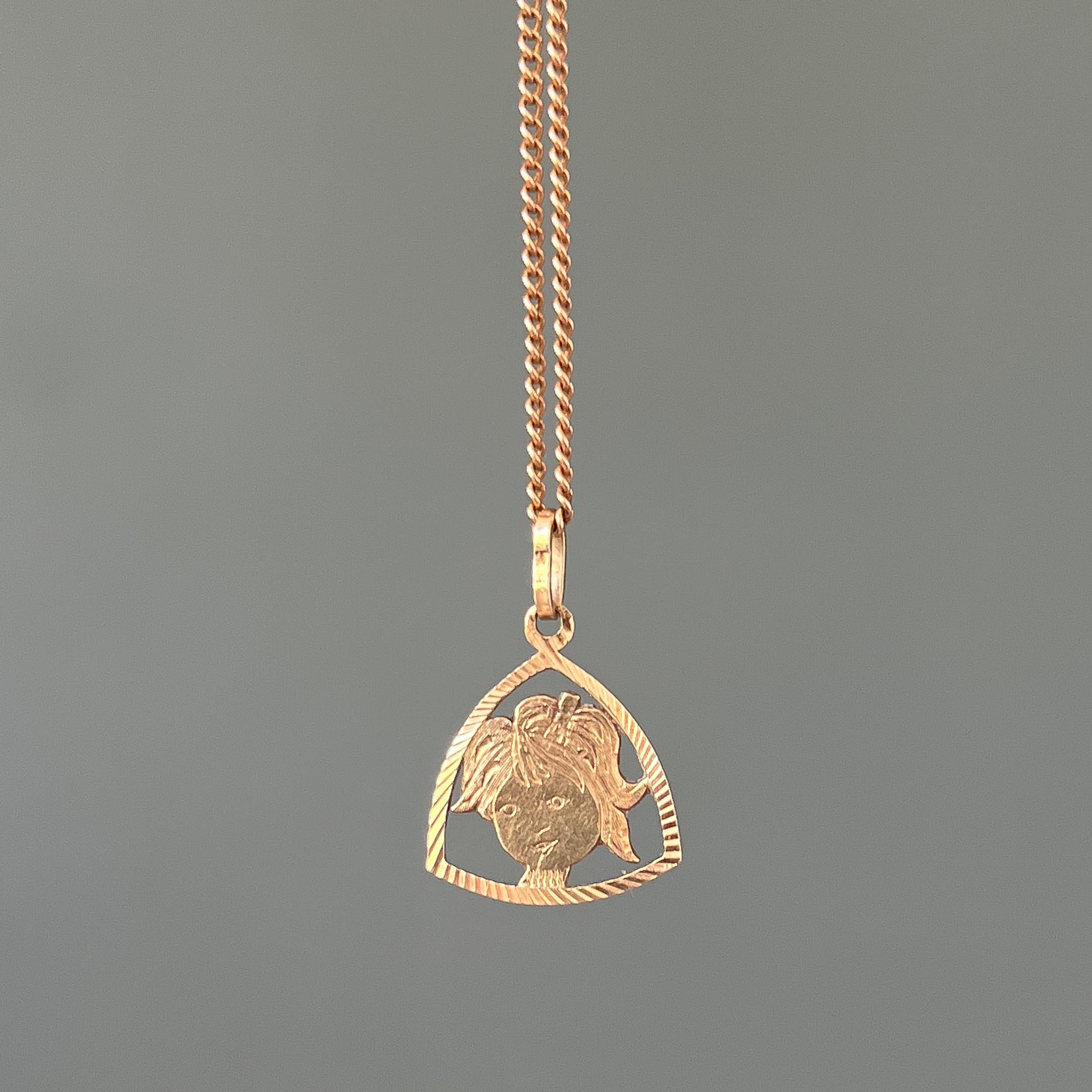 A charm pendant depicting a girl in a 14 karat gold stirrup frame. This vintage charm has a beautiful design with engraved grooved details on the border. The little girl has a lovely smile on her face and a bow wrapped in her hair.

Charms are great