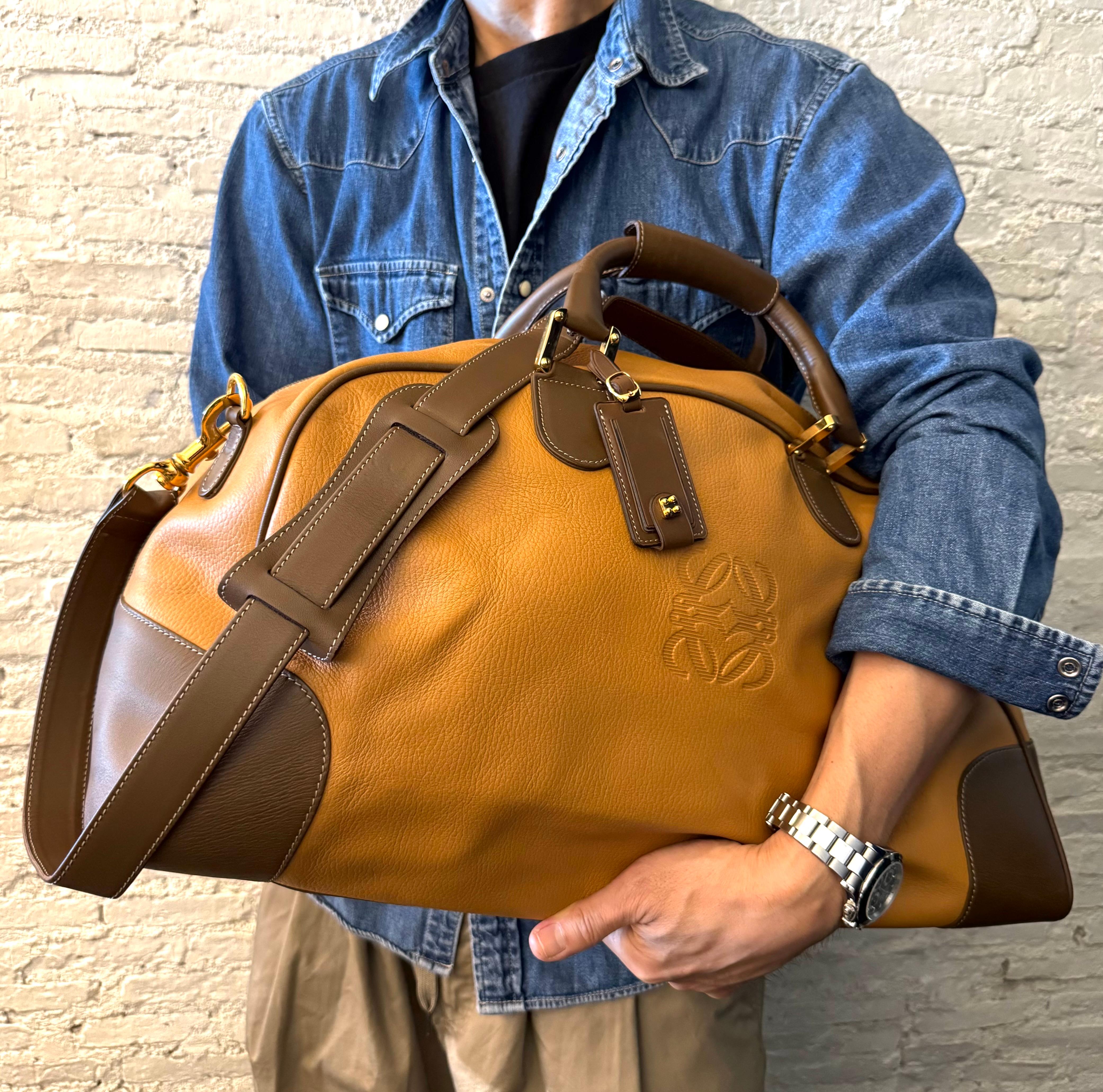 This vintage LOEWE Anagram XL boston bag is crafted of large-grained calfskin leather in mustard yellow trimmed with smooth calfskin leather in brown featuring gold toned hardware and rolled leather handles. Top zipper closure opens to an unlined