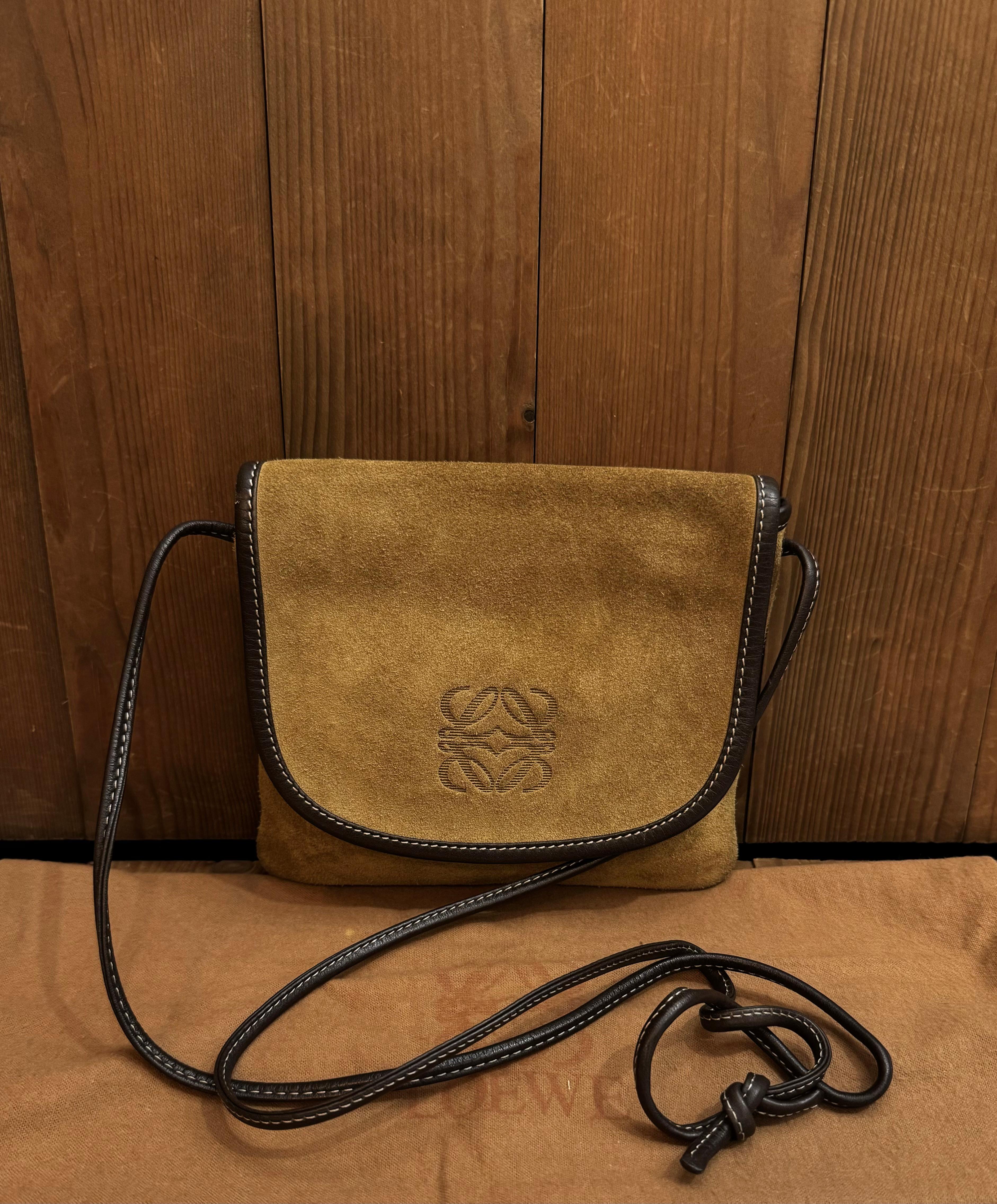 This vintage LOEWE Anagram mini flat crossbody bag is crafted of brown calfskin suede and leather featuring gold toned hardware and a  crossbody drawstring strap crafted of the same leather. Front flap with zipper closure opens to an unlined