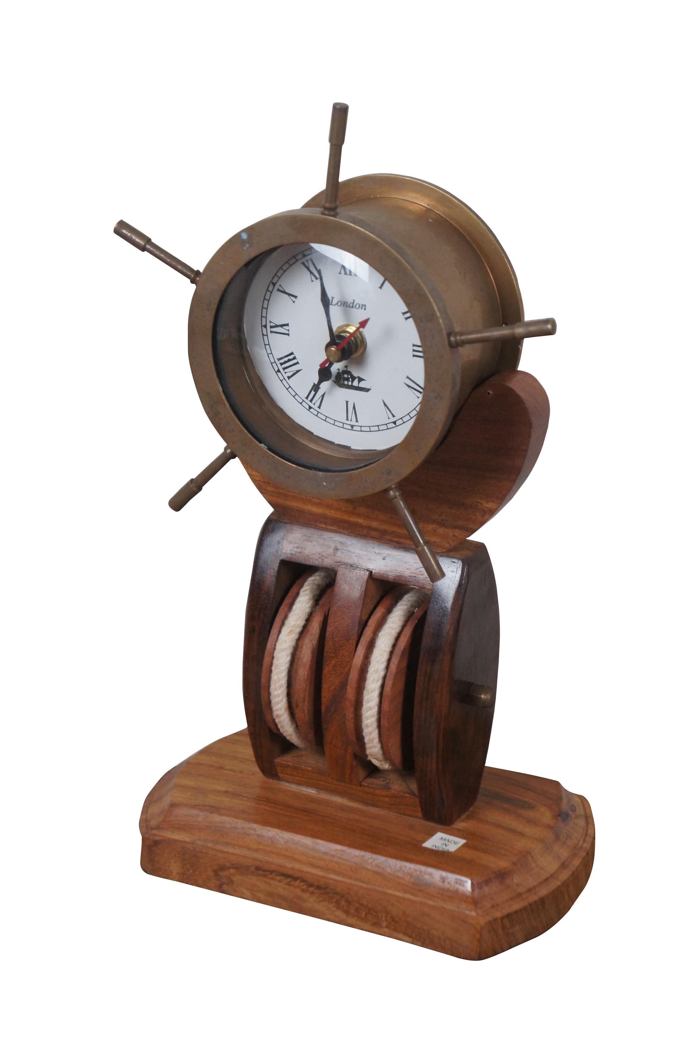 Late 20th century desk clock in the shape of a brass ship's wheel / helm, mounted on a wooden double pulley base. White face with Roman numerals, marked London. Prestige Quartz battery operated movement. Made in India. 

Dimensions:
6.75