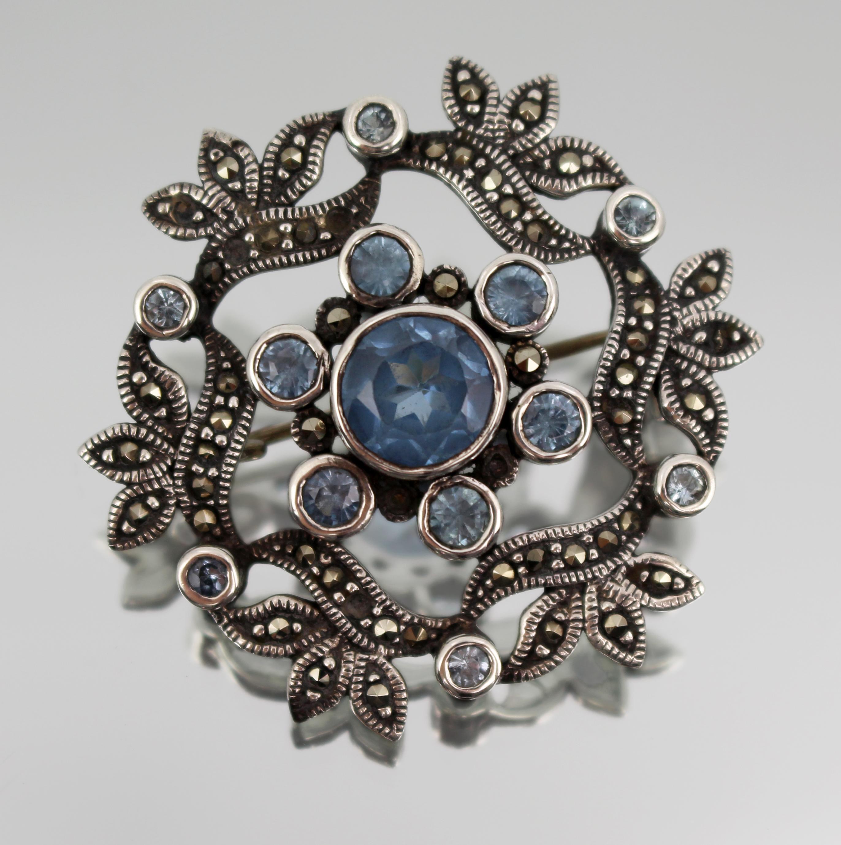 Vintage London Silber, Markasit & Blaustein Brosche, 1978

Eine fein gearbeitete Brosche aus Sterlingsilber in kreisförmiger Form mit einem blauen, facettierten Stein in der Mitte, umgeben von acht passenden Steinen und mit Markasiten besetzten