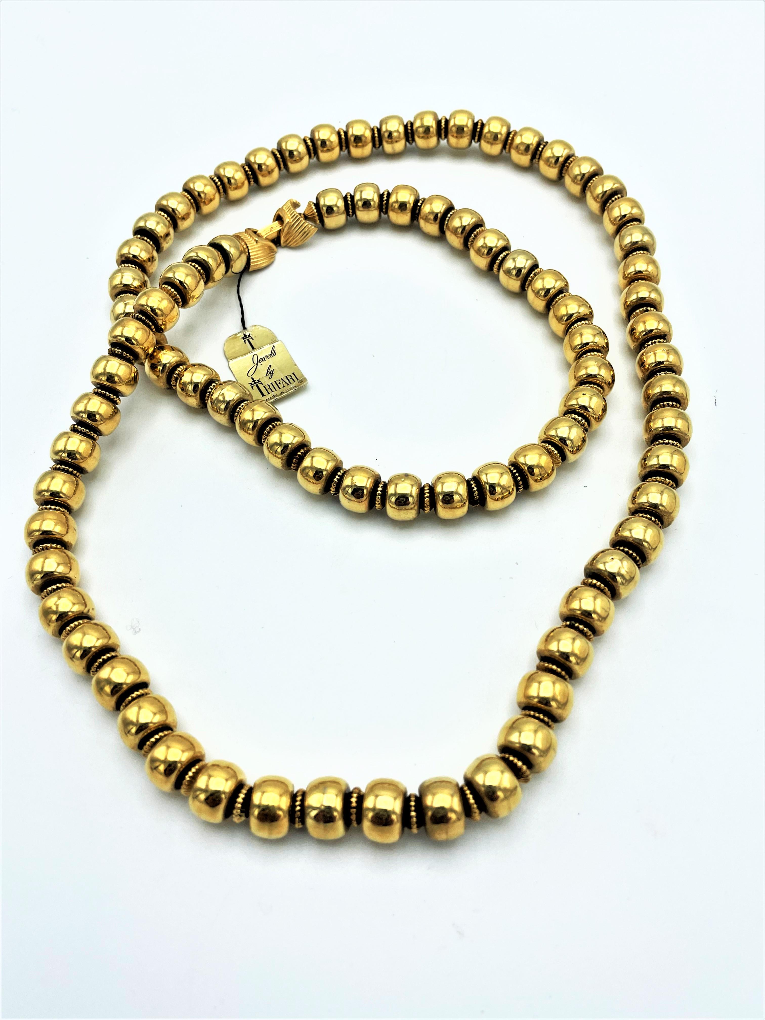 Long chain consisting of gold-plated balls that are flattened on the sides, with small serrated discs in between. The necklace has never been worn as the original 'Jewel of TRIFARI' label is still attached to the beautiful clasp. The balls are