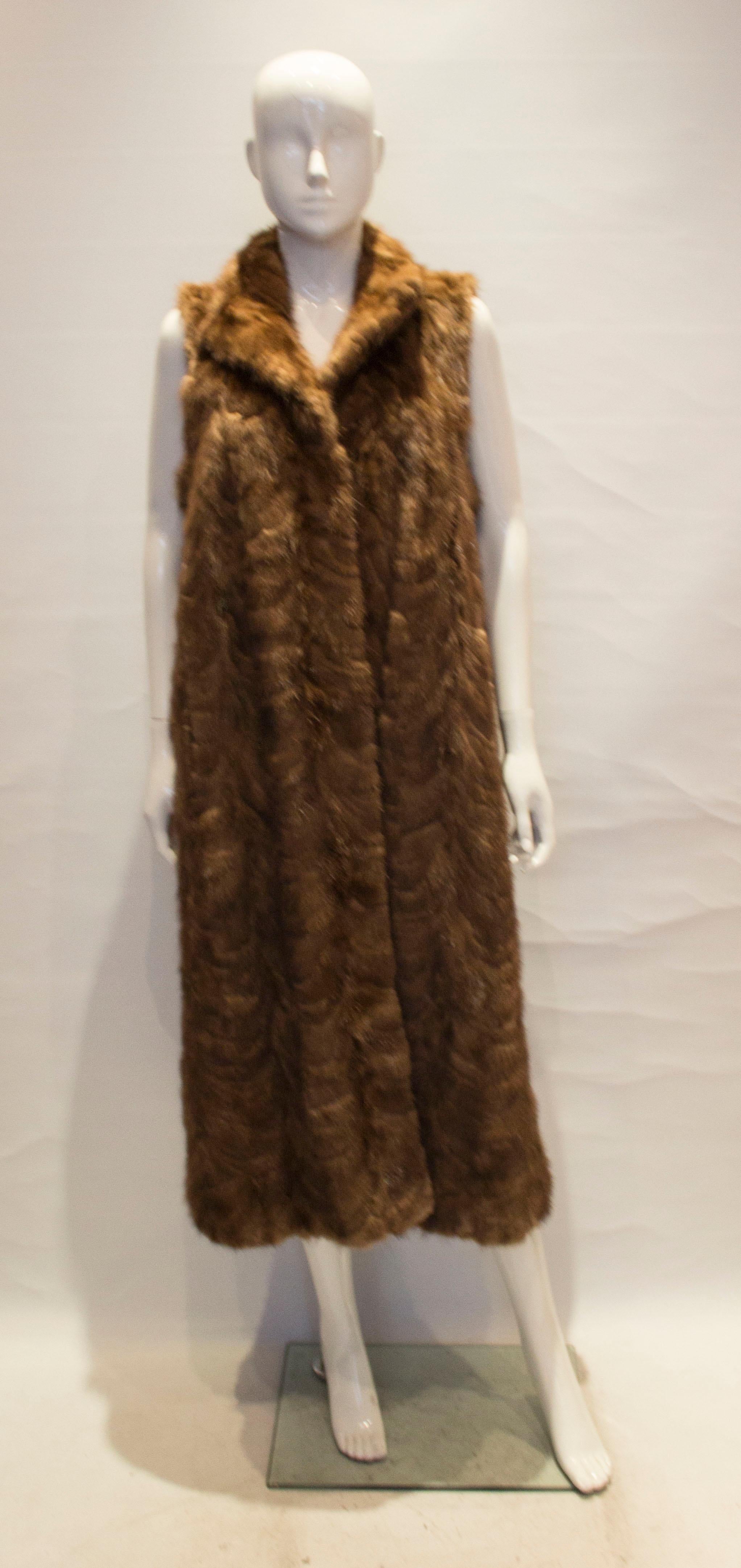 A chic and easy to wear long mink gilet , in a brown caramel colour. The gilet has a collar neckline, hook and eye fastening at the front and a pocket on either side. 