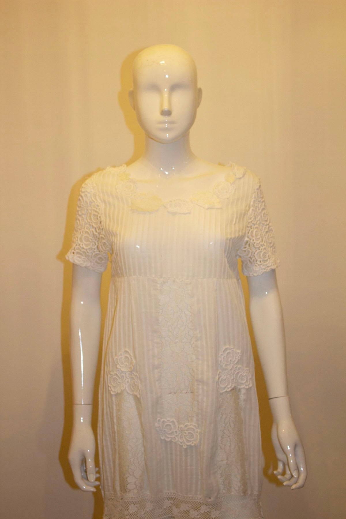 An elegant and easy to wear white summer gown, or possible wedding dress. The dress is column style and fits over the head, though a zip could easily be added. It has lace sleaves , vertical pin tucks  and a gap in the hem to aid walking.