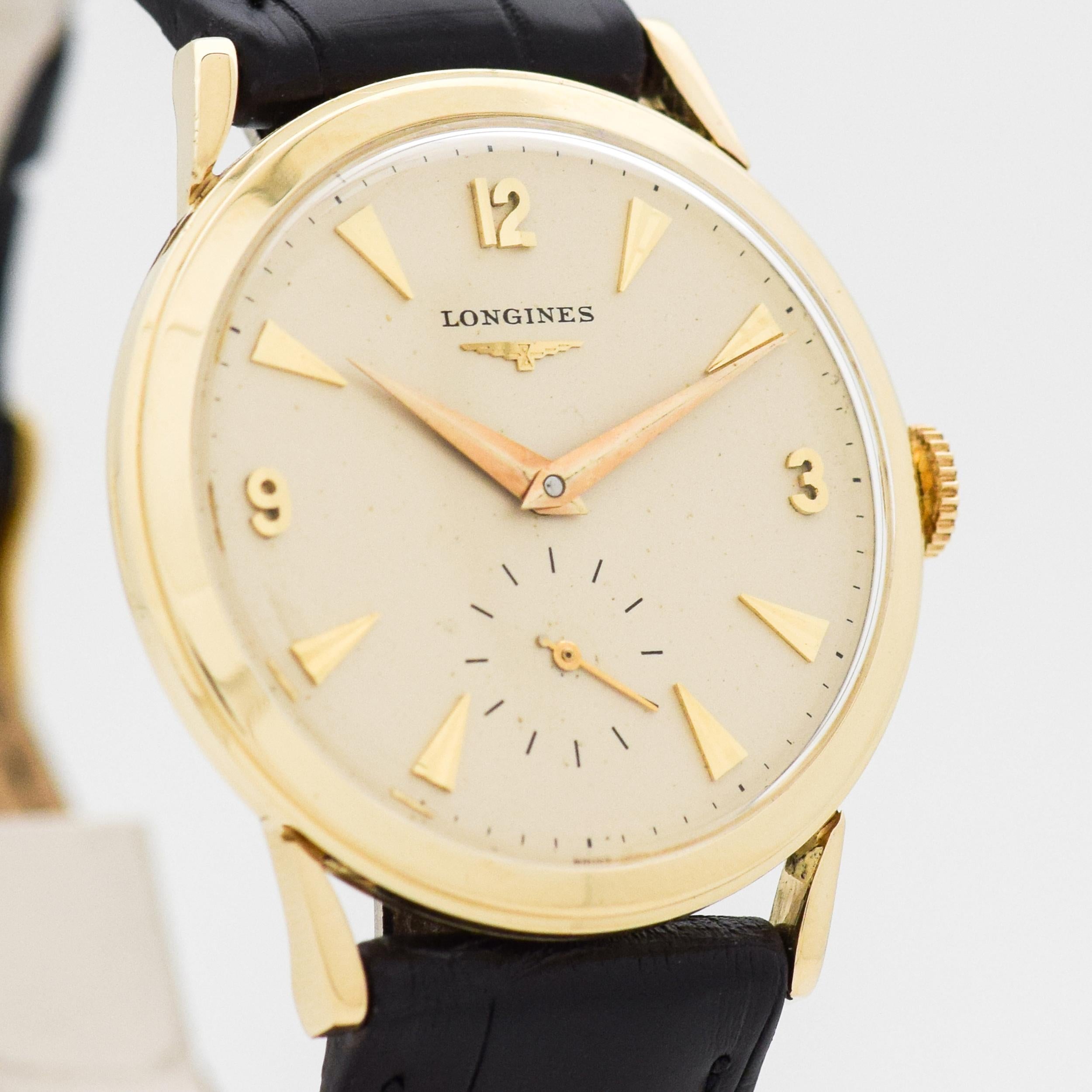 1958 Vintage Longines Watch. 14K Yellow Gold case. Original, silver dial with applied, yellow gold-colored Arabic numerals & arrow markers. 32mm wide. Equipped with a 17-jewel, manual caliber movement. Featured on a Genuine Alligator Matte Black