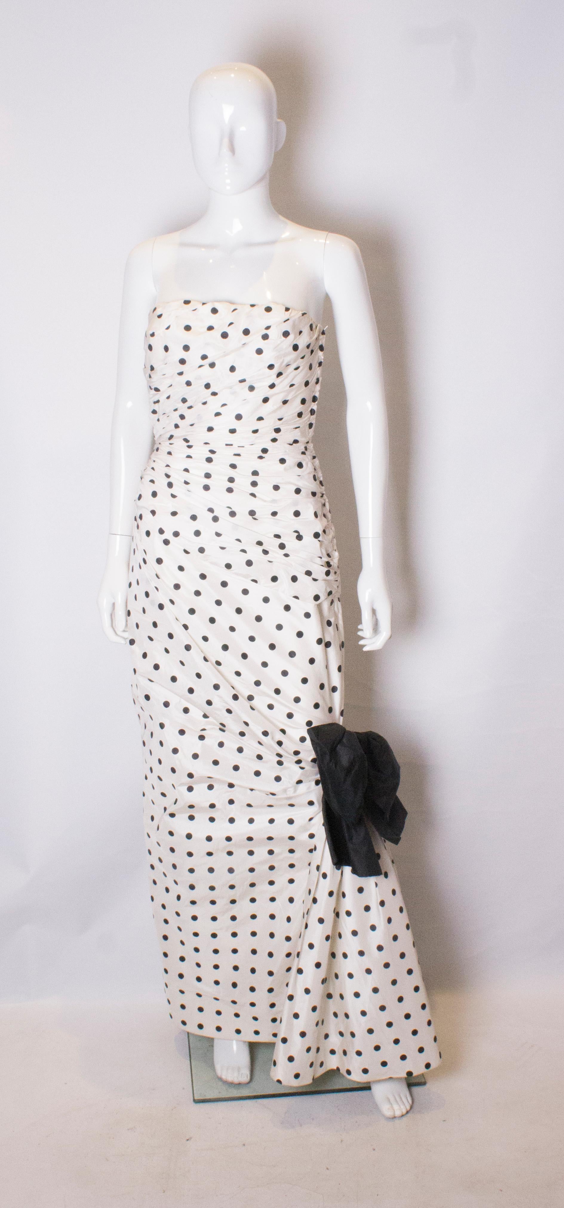  A real headturner of a gown. This strapless evening gown by Lorcan Mullany, is 100% silk with a white background and black spots.  It is gathered and has a side zip opening, with a black silk bow at knee leval.
Measurements: bust 35'', waist 27'',