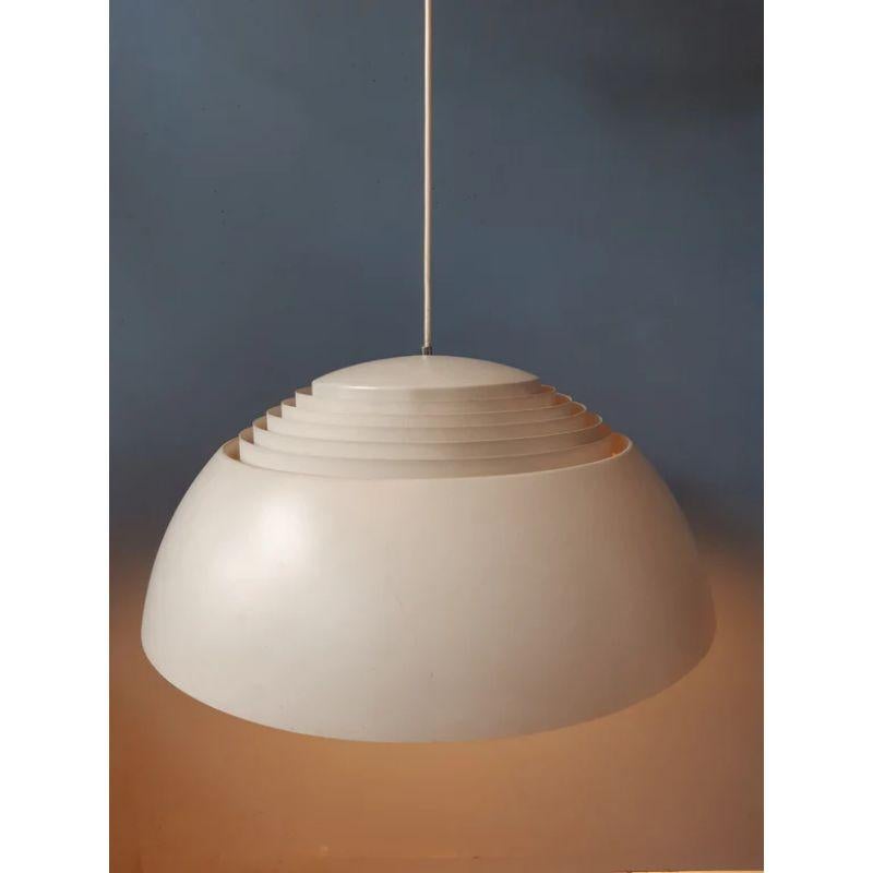 Pendentif classique Louis Poulsen AJ Royal conçu par Arne Jacobsen en couleur beige/blanc/gris. La lampe est en métal et se compose d'un abat-jour intérieur et extérieur. Les lamelles du design reflètent magnifiquement la lumière. La lampe nécessite