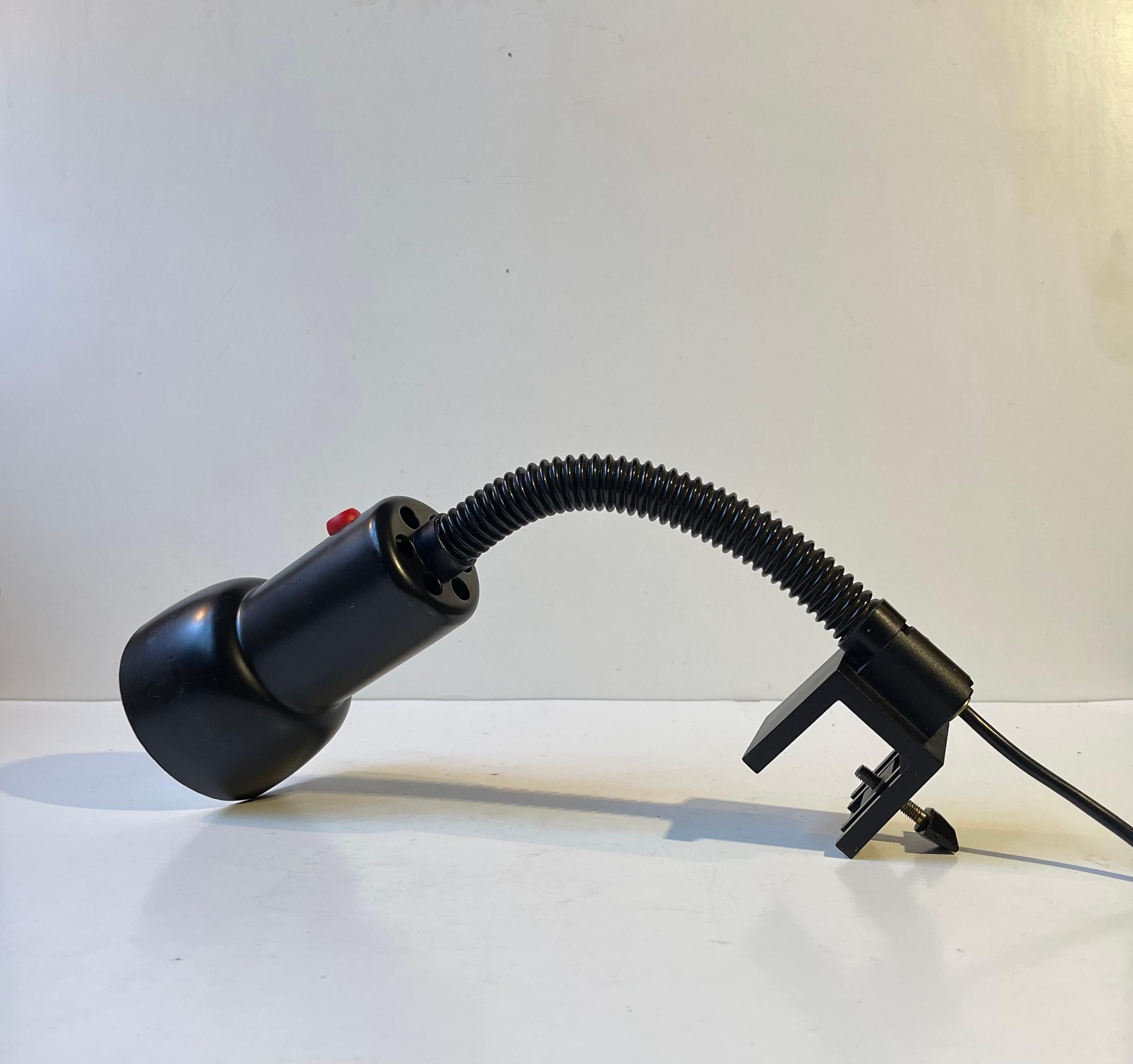 Aplique multiajustable con soporte de pinza. La luz puede dirigirse en cualquier dirección. Todo es negro, excepto el interruptor rojo de encendido y apagado. Se llama Louis Poulsen negro y fue fabricado por Louis Poulsen en Dinamarca durante la