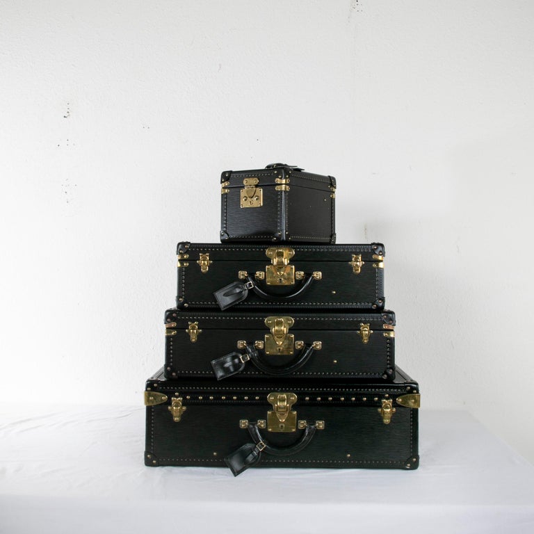 This stunning set of vintage Louis Vuitton black epi leather luggage features three suitcases and one cosmetic case. Detailed with brass studs and corners, each suitcase includes its original pair of keys. The brass locks are stamped Louis Vuitton,