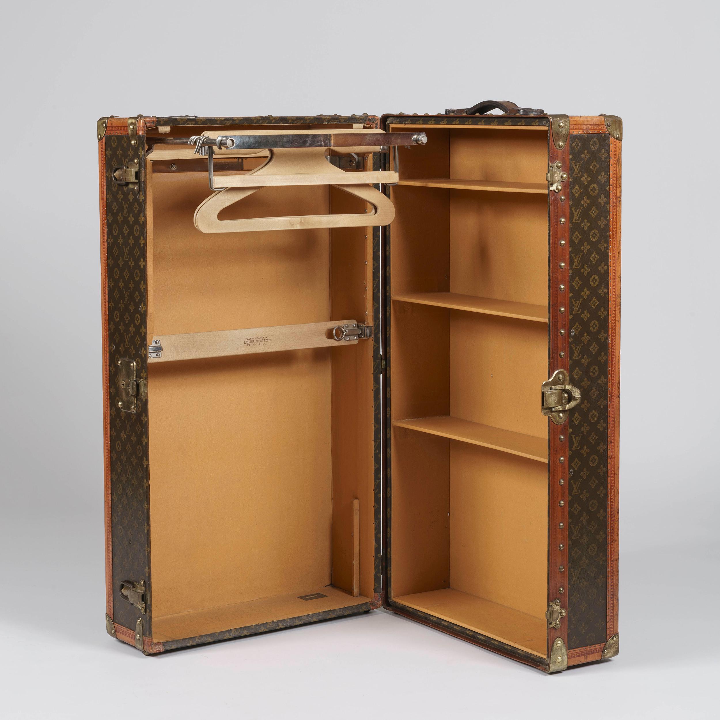 A Louis Vuitton Cabin Trunk

Constructed in wood and monogrammed canvas and edged with brass guards, triple hinged, opening to reveal a tan leather lined interior, one side fitted with wooden hangers on a chrome plated double rail, with a clothes