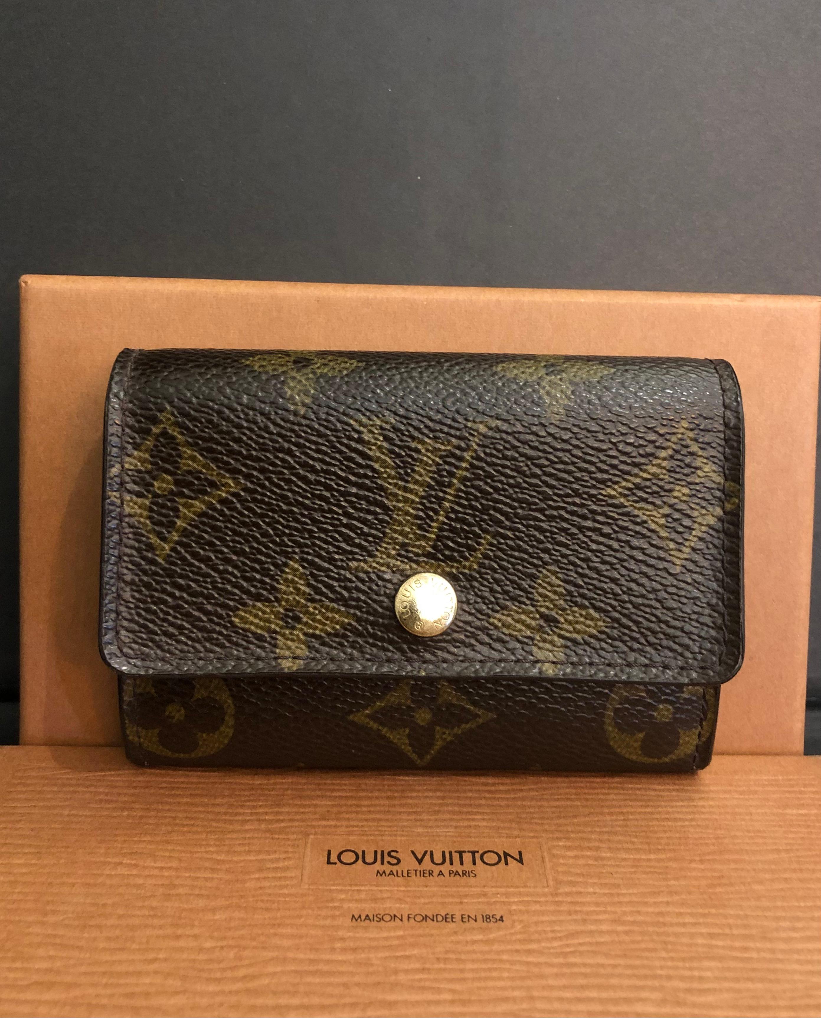 This vintage LOUIS VUITTON card holder is crafted of LOUIS VUITTON coated monogram canvas and brass hardware. Front flap snap closure opens to two main compartments lined with textured and smooth leather featuring a front patch pocket. Measures