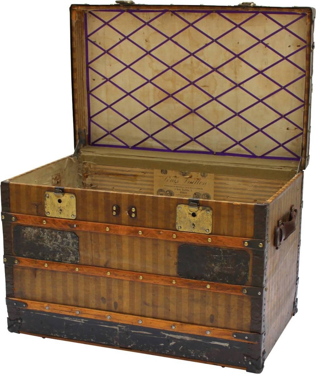 A stately Louis Vuitton courier trunk of an early vintage due to its covering in the traditional red and beige striped canvas design. Beautiful brass hardware and timber slats fastened with extra-large brass buttons add to its allure. The interior