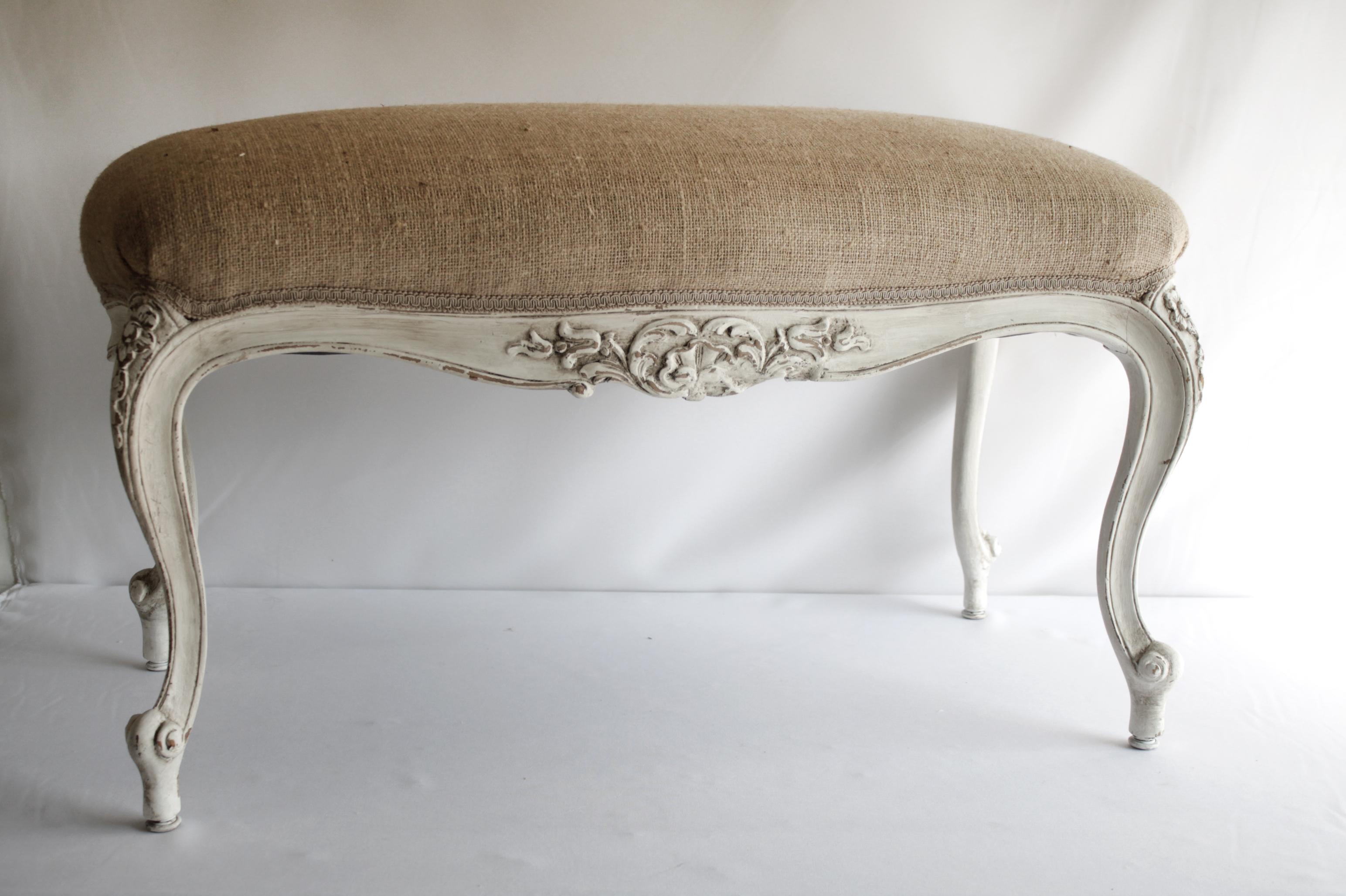 Vintage Louis XV style burlap upholstered bench or ottoman.
Painted our antique white patina, and upholstered with a burlap seat. Classic cabriole style legs with carved floral details at the top of each leg. The longer sides have a carved