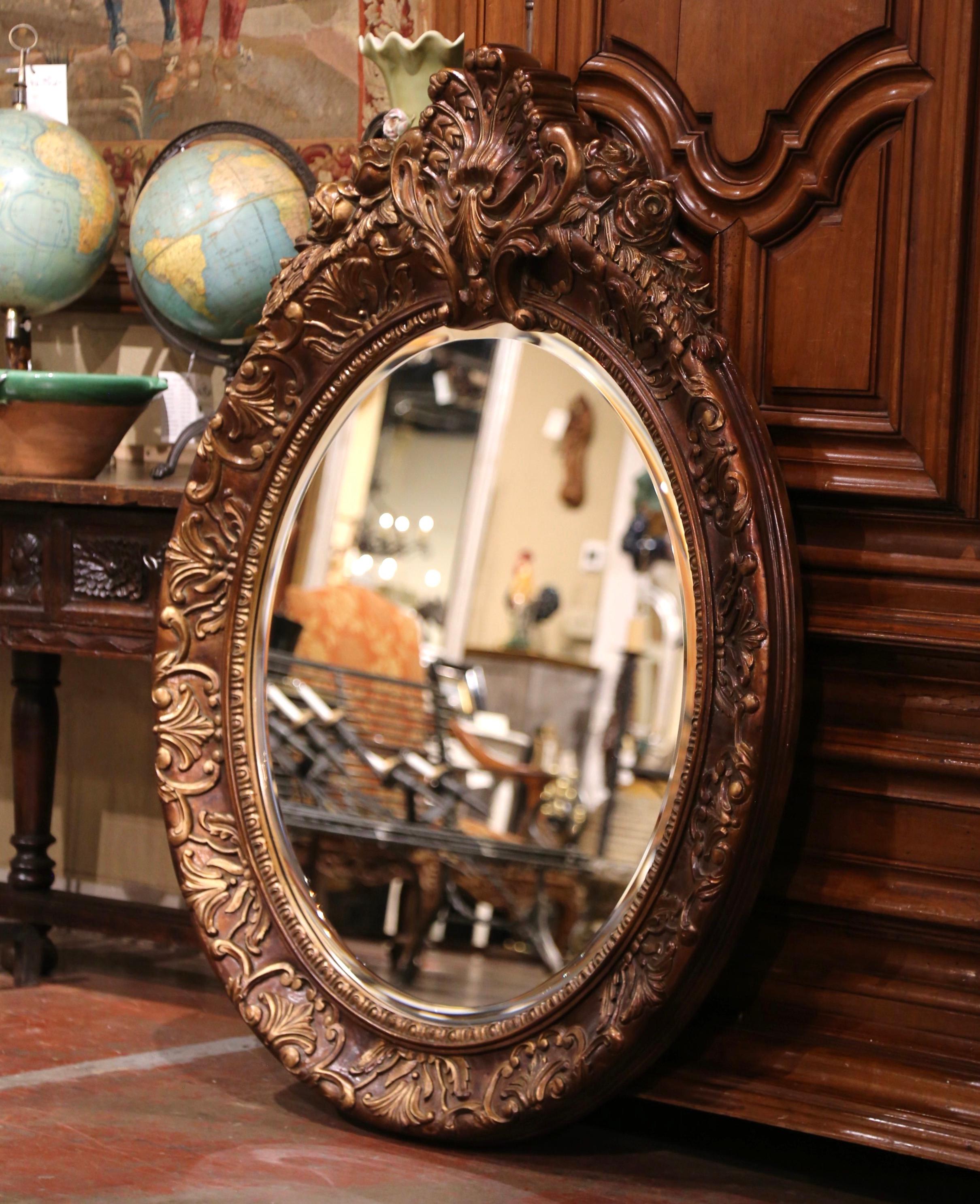 Oval in shape, the mirror features a decorative shell cartouche flanked with foliage decor, discrete engraved floral and rose motifs around the frame and another intricate shell motif in high relief at the bottom; the frame is further embellished