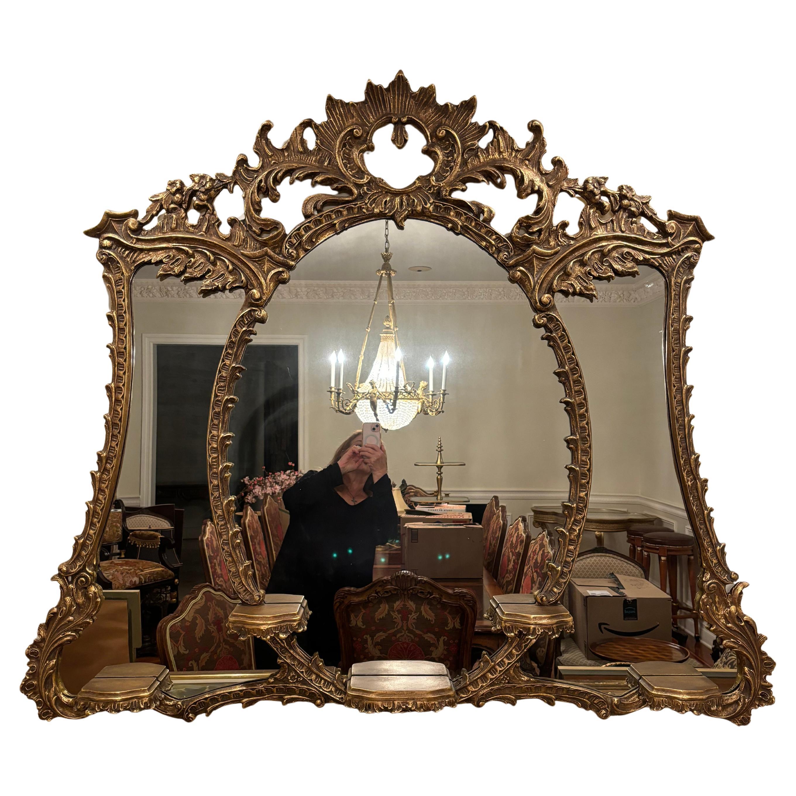 Elegante specchio intagliato in legno dorato in stile Luigi XV di Friedman Brothers con corona con conchiglia aperta e intagli sulla parte superiore. Intorno allo specchio ovale centrale ci sono gli stessi intagli che incorniciano gli specchi