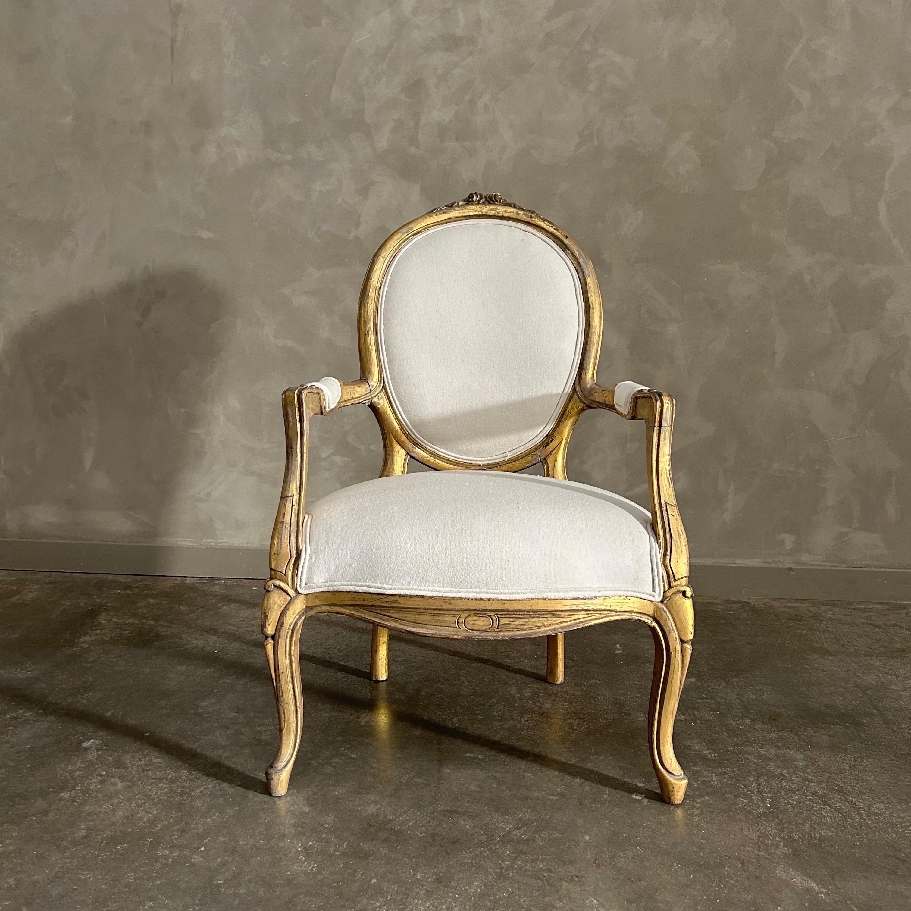Vintage gilt wood open arm chair. This vintage chair has the original finish, which is a weathered patina gilt wood. We have reupholstered them in a linen with burlap back.  Finished each by hand for a true antique look. Solid and sturdy, petite,