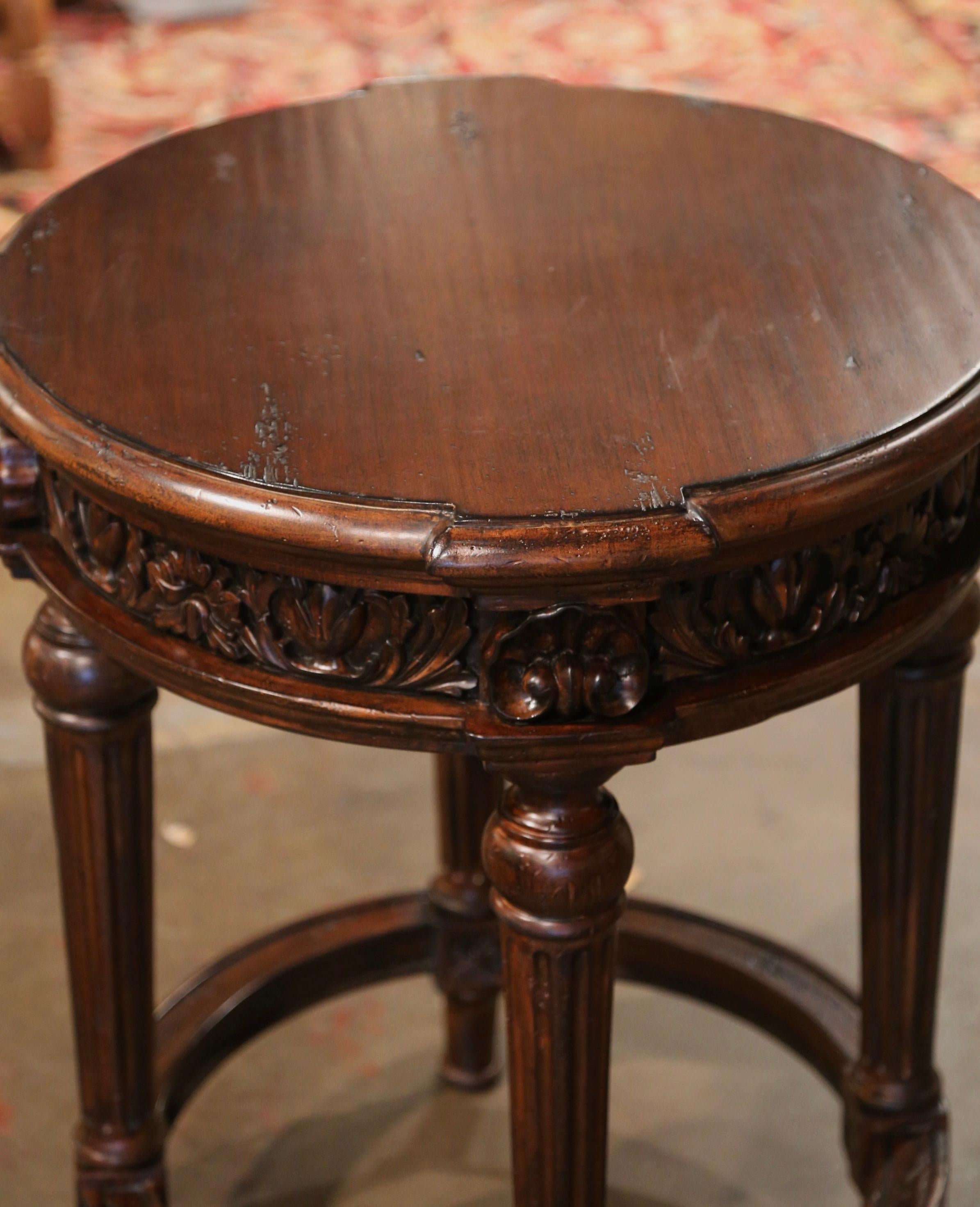 Use this elegant, antique fruit wood table in a living room or den as an occasional side table. Crafted by Habersham Co. circa 1980, the round table stands on four tapered and fluted legs, dressed with a bottom stretcher, over a heavily carved apron