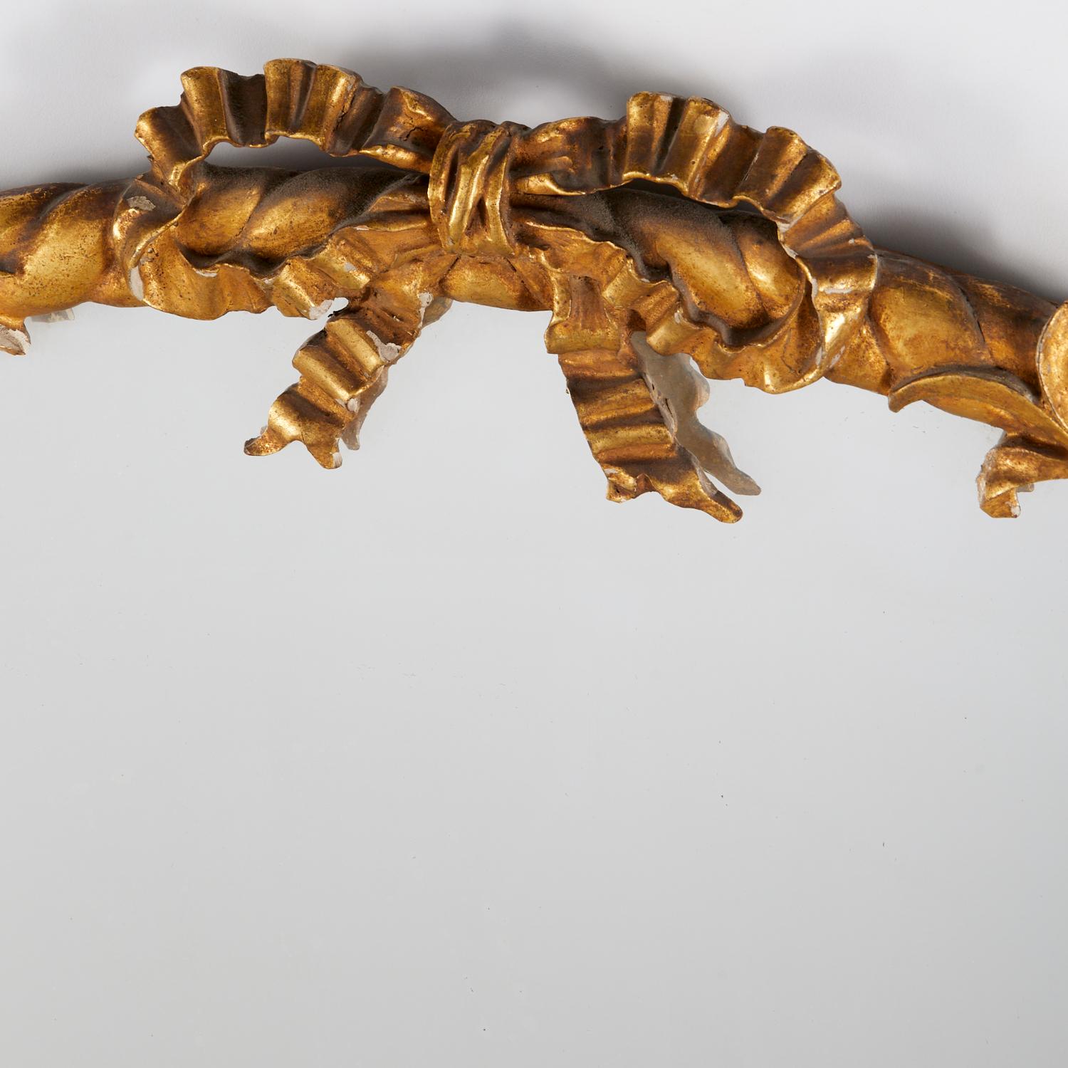 Primera mitad del siglo XX, Italia, precioso espejo de madera dorada de estilo Luis XVI. El espejo tiene forma de gran cesta de flores con cresta de lazo atado, el asa de la cesta está entrelazada con una enredadera asimétrica serpenteante. El