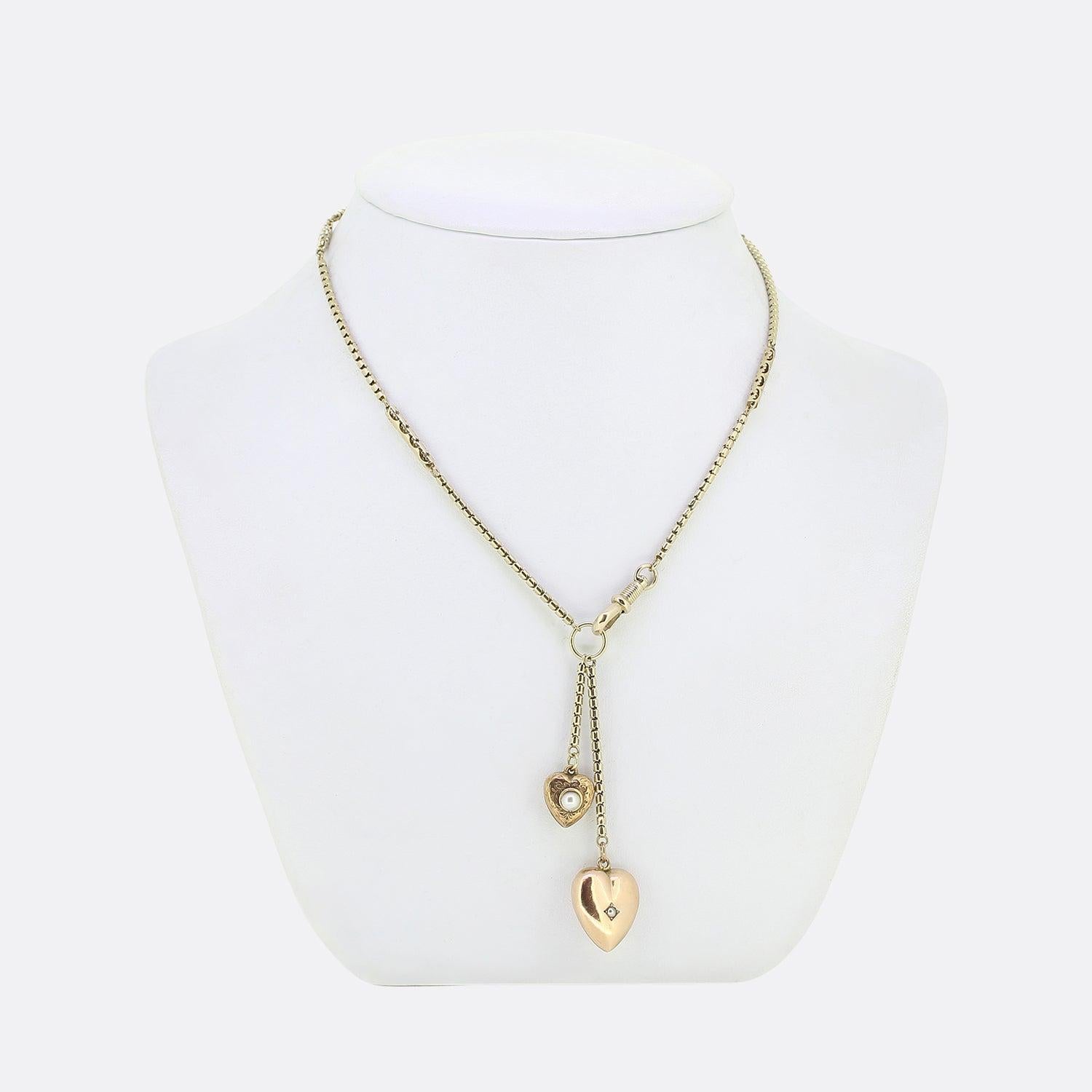 Here we have a vintage 9ct yellow gold charm necklace. An antique boxed chain with ornate pierced work plays host to two freely hanging love heart pendants below. The largest of which showcases a plain polished finish with a single seed pearl to the