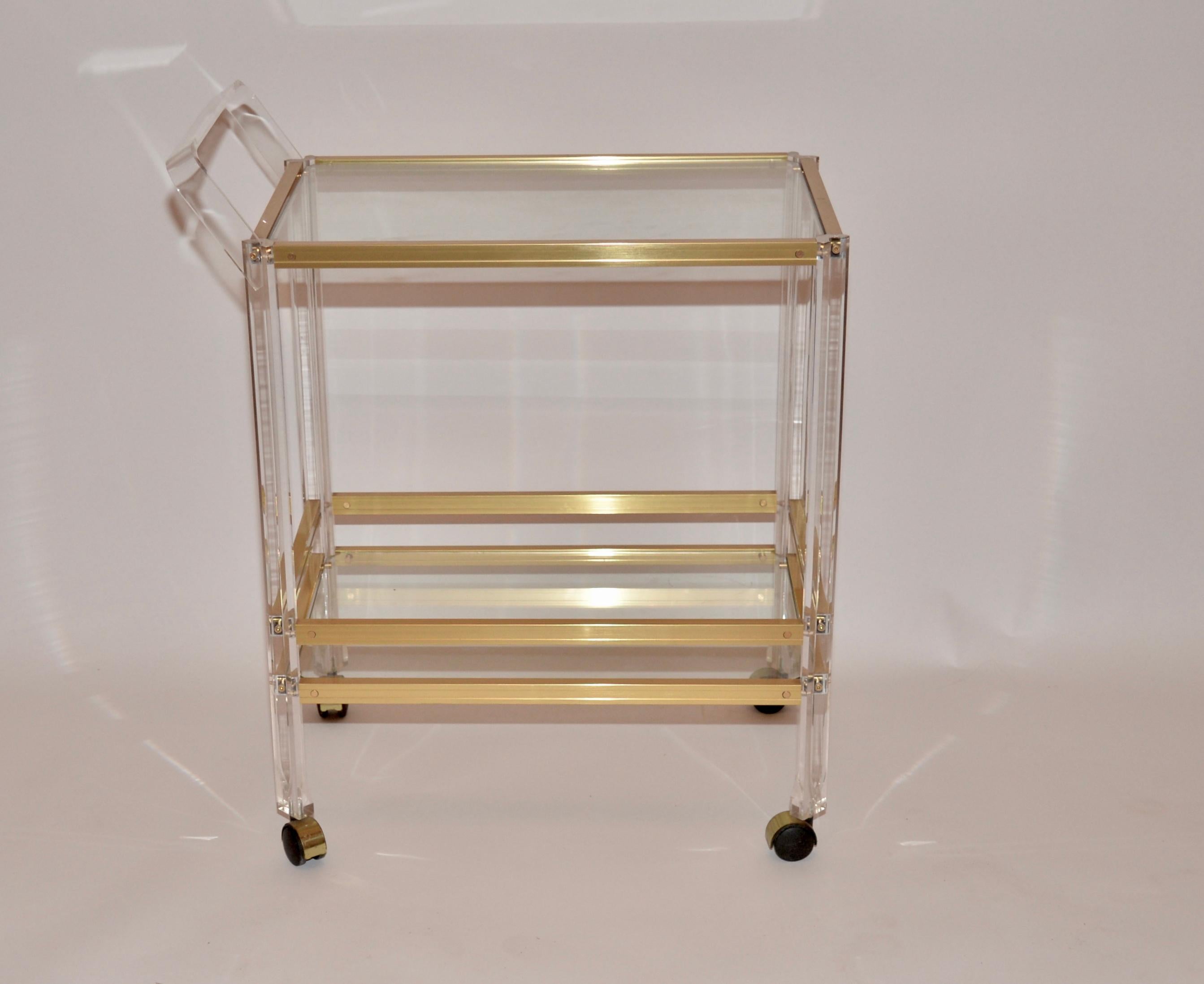 An original 1980s vintage glass and Lucite drinks or serving trolley. Two tiers of glass shelving and a Lucite frame incorporating a brass effect finish.