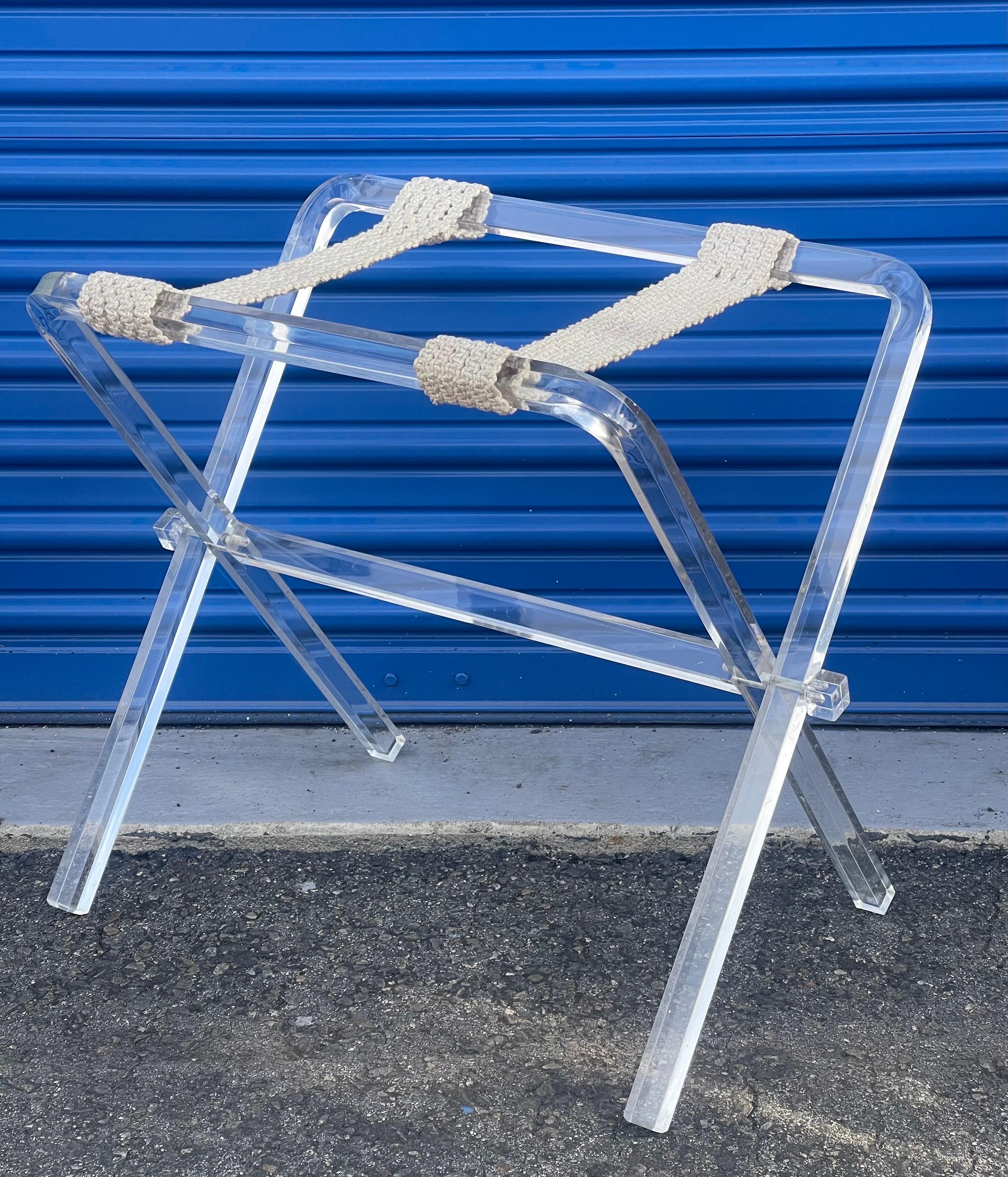 A really nice vintage lucite and macrame folding luggage rack by Creations At Dallas, circa 1970s.  The piece features two white macrame straps on a folding lucite base. The luggage stand is marked ‘Creations at Dallas’ to the lower part of one of