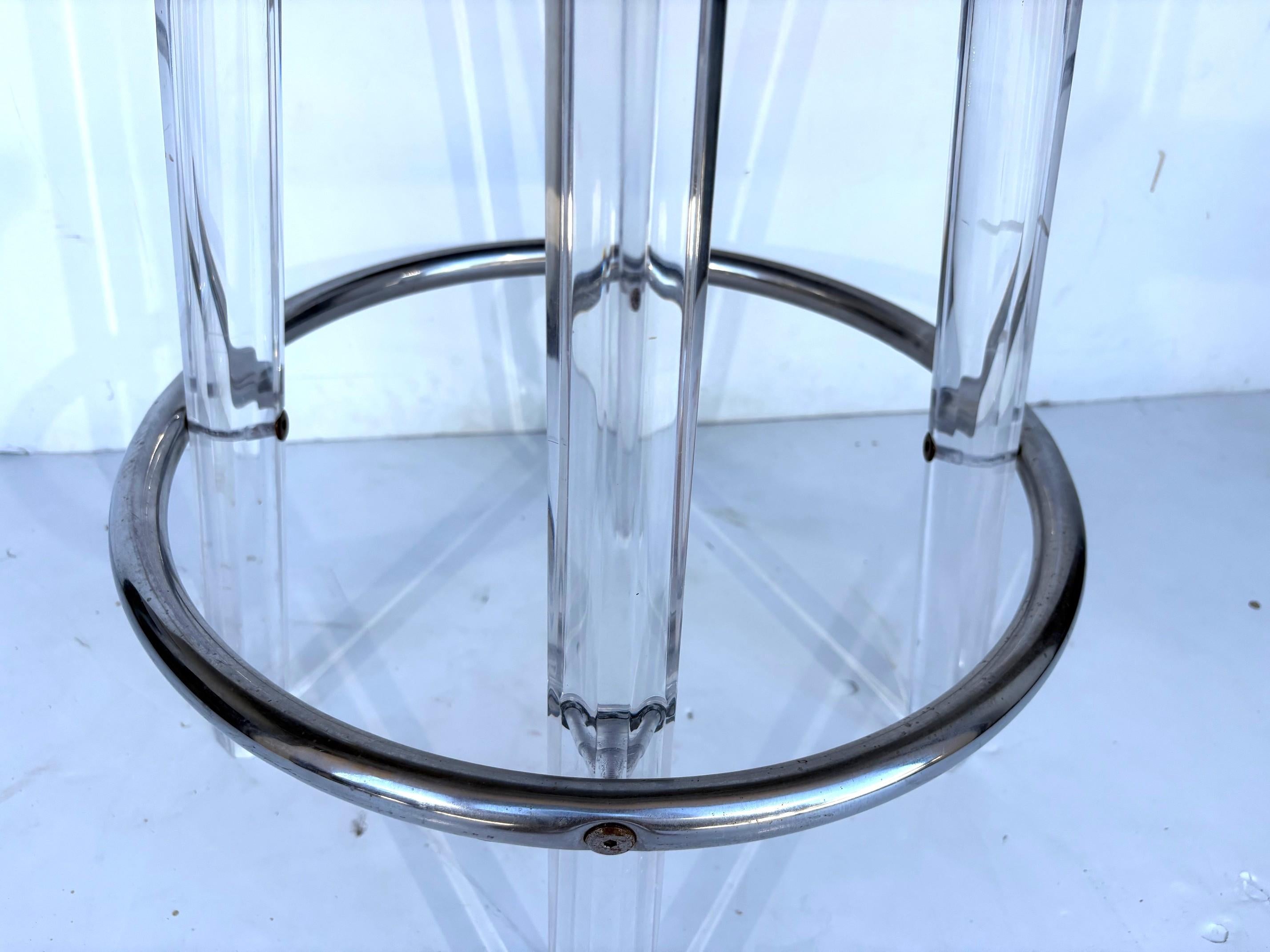 A set of three lucite barstools. The stools have three lucite legs, a round seat that swivels, and a chrome stretcher. 