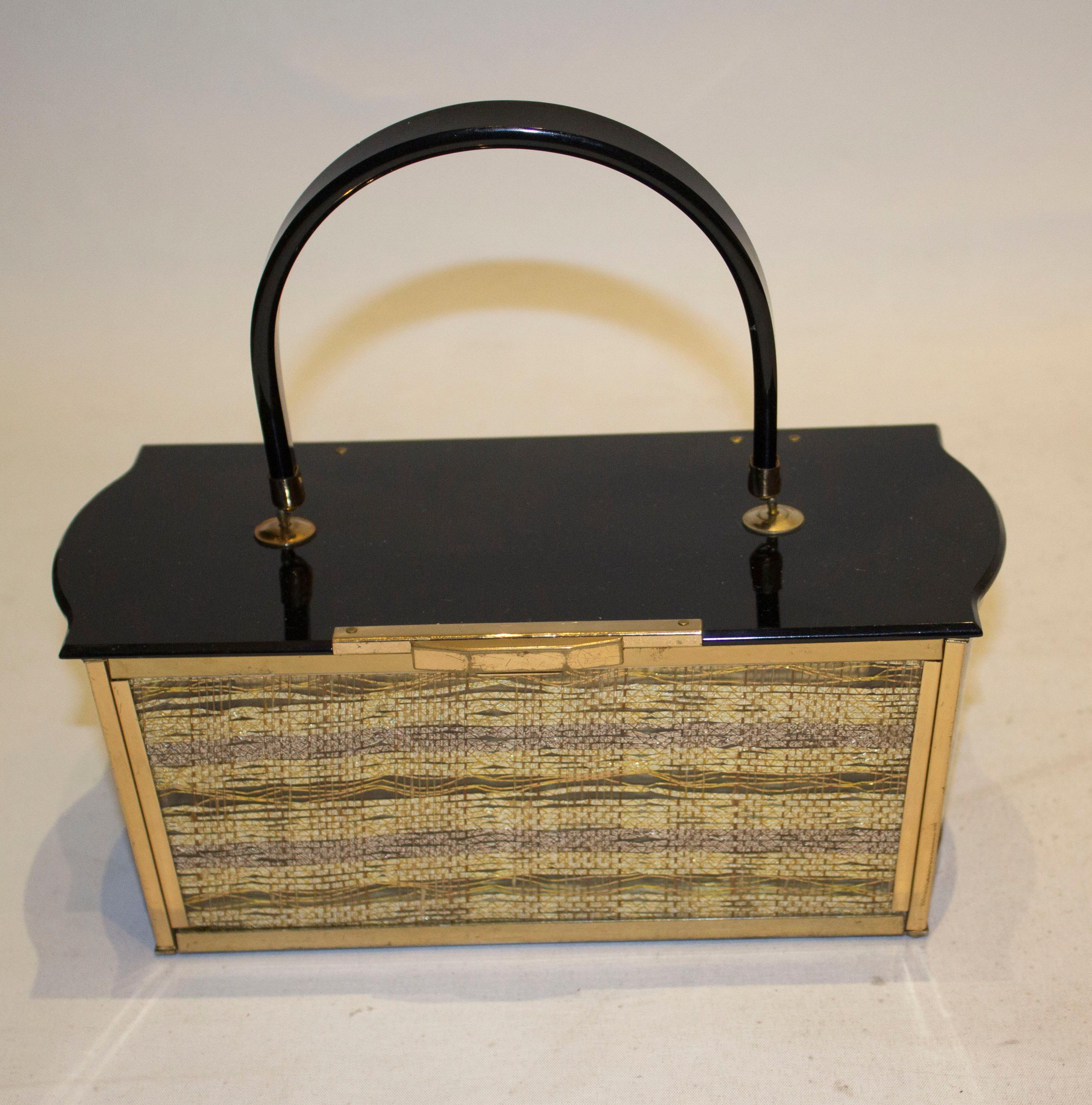 A chic black and gold lucite evening bag with top handle. The bag has a black lid with woven gold and bronze sides. width 10'', depth 5'' , height 4''.