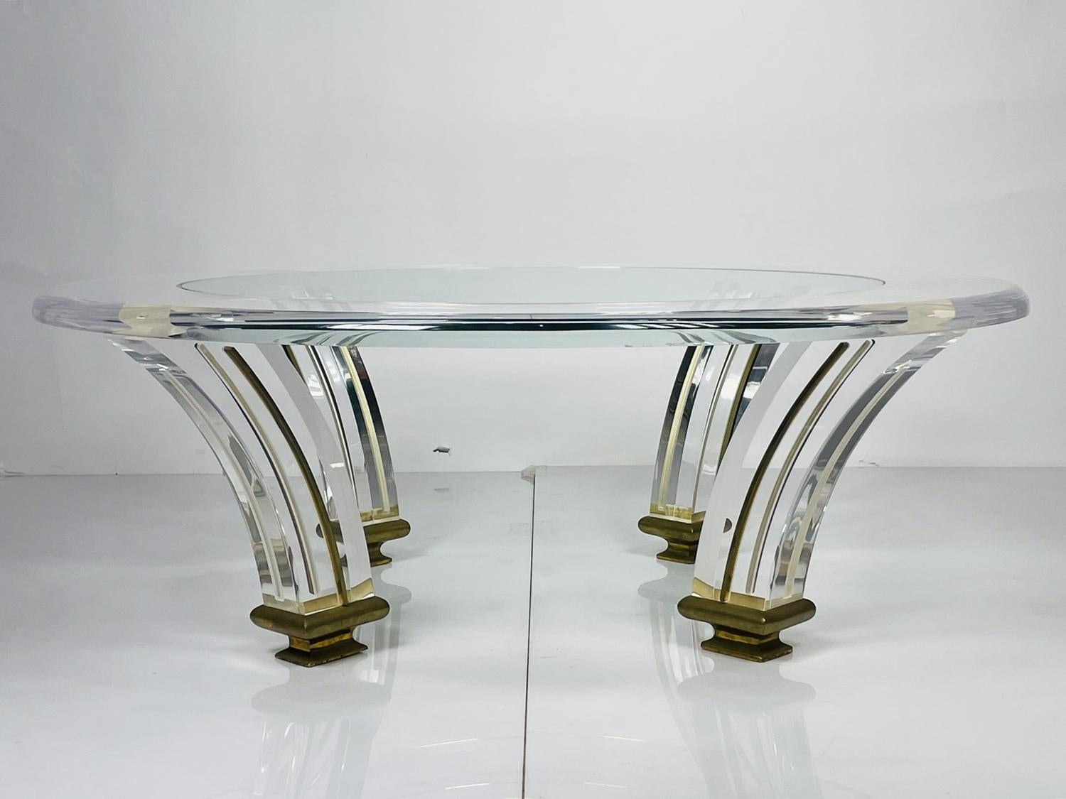 Vintage coffee table executed in Lucite, brass and glass.
The base has a splayed tusk shaped legs with brass detail running up the legs and solid brass rounded caps at the bottom of the legs.
The top is made of a a thick Lucite with bullnose edge