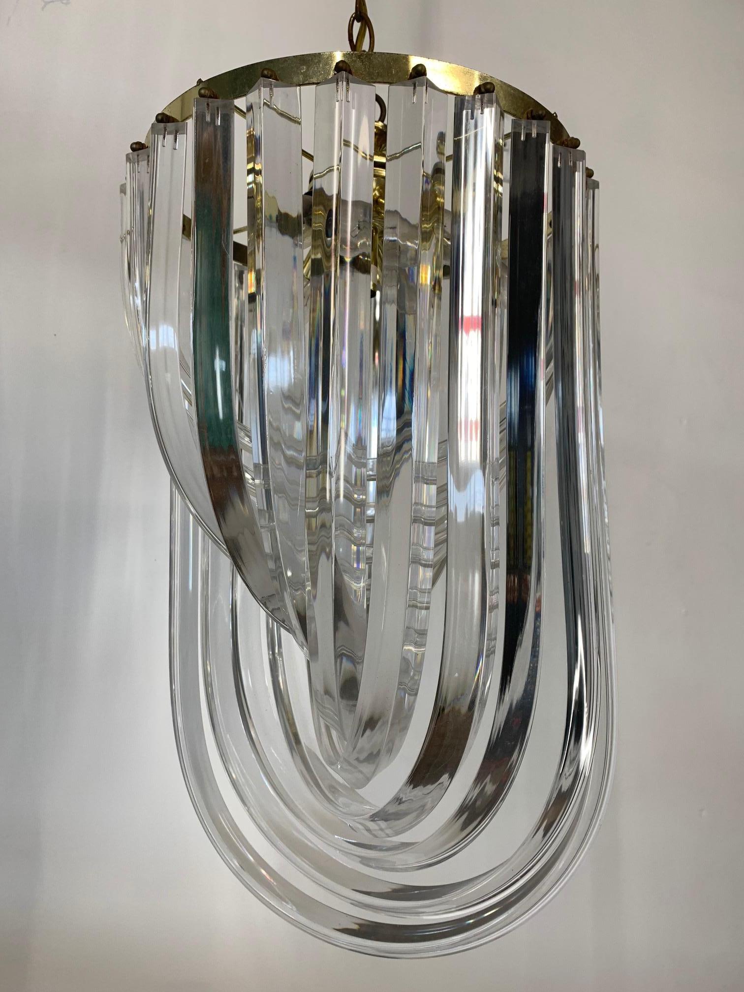 Vintage Lucite hoop chandelier features large ribbon style hoops and brass accents. Takes six chandelier style bulbs. Moderate patina as shown but does not distract from beauty of fixture.