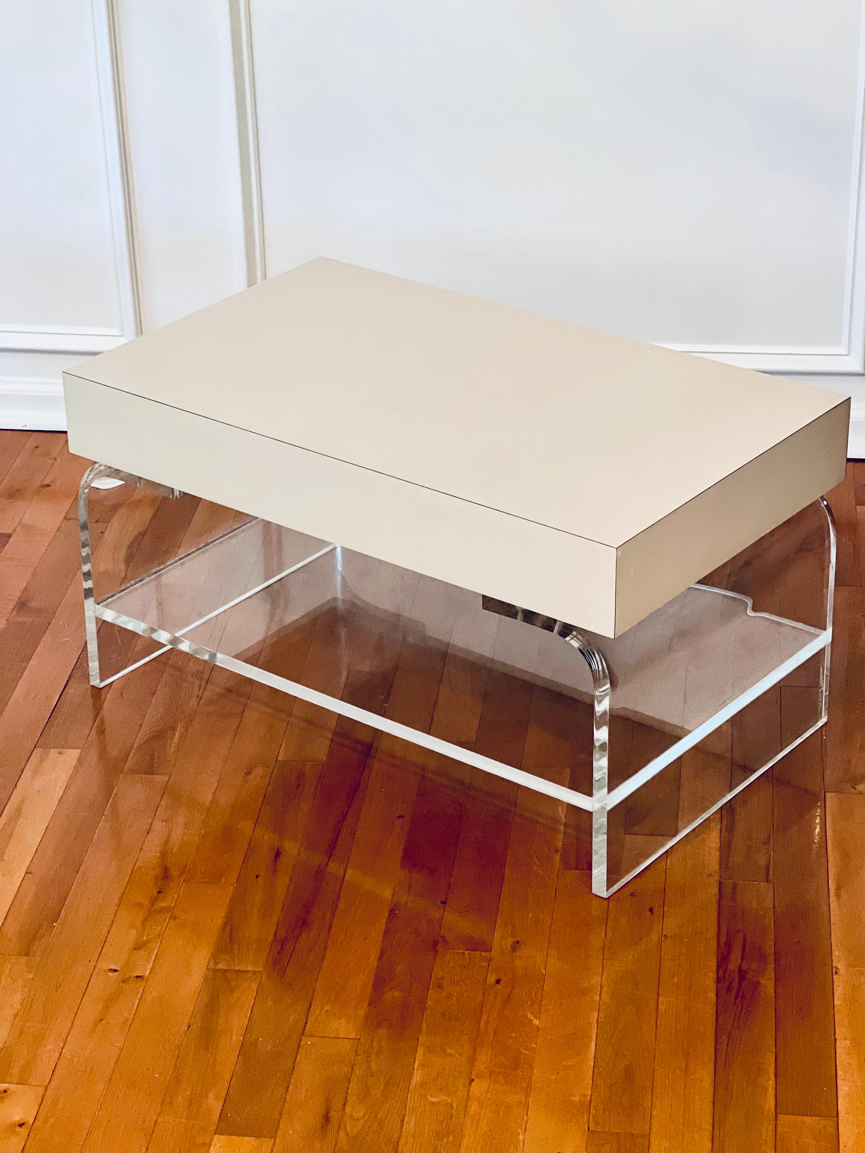 Vintage lucite waterfall coffee table with a laminate top, circa 1970-80's.

Chic little table with a high quality lucite base and lower shelf with a faux monolith slab top in a vibrant cream laminate. It may be used as a small coffee table or side
