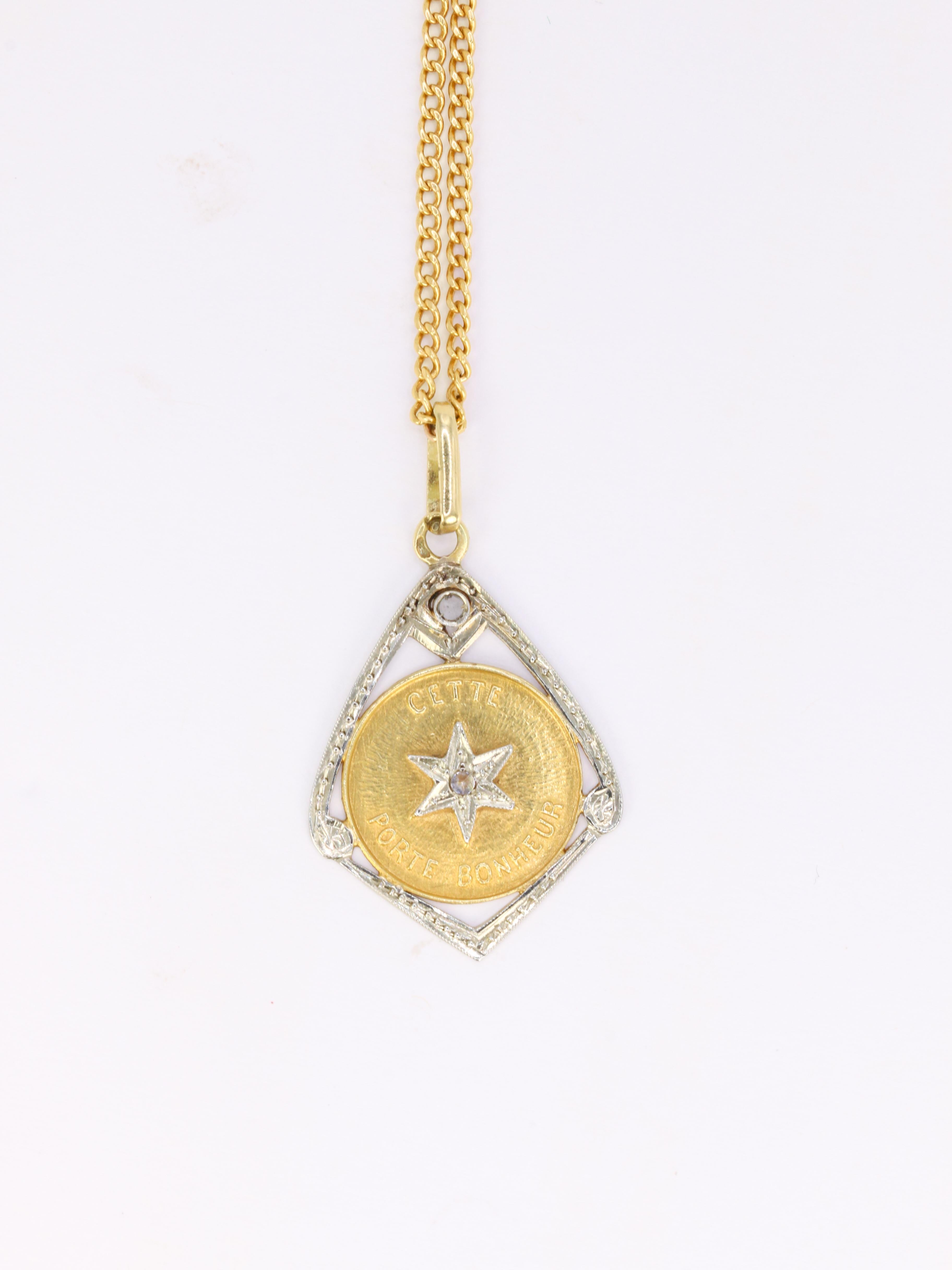 18Kt (750°/°°) yellow and white gold lucky star pendant set with a rose-cut diamond.
The pendant is composed of a diamond-shaped frame set with a small rose-cut diamond and a round medal featuring a rebus 