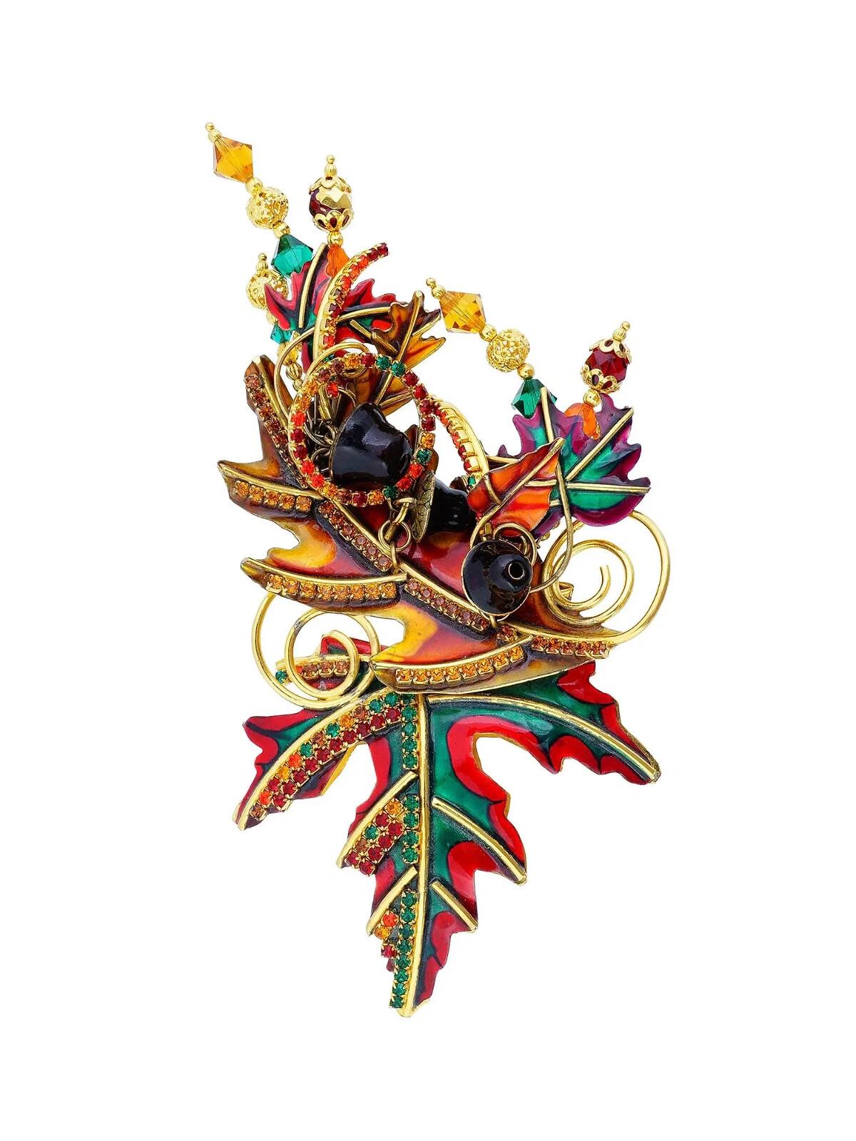 A vintage Lunch at The Ritz costume jewelry pin brooch. The brooch showcases a design featuring swirling gold tone metal and autumnal hues. A rich blend of reds, greens, and golds, reminiscent of fall foliage. The brooch is adorned with a cascade