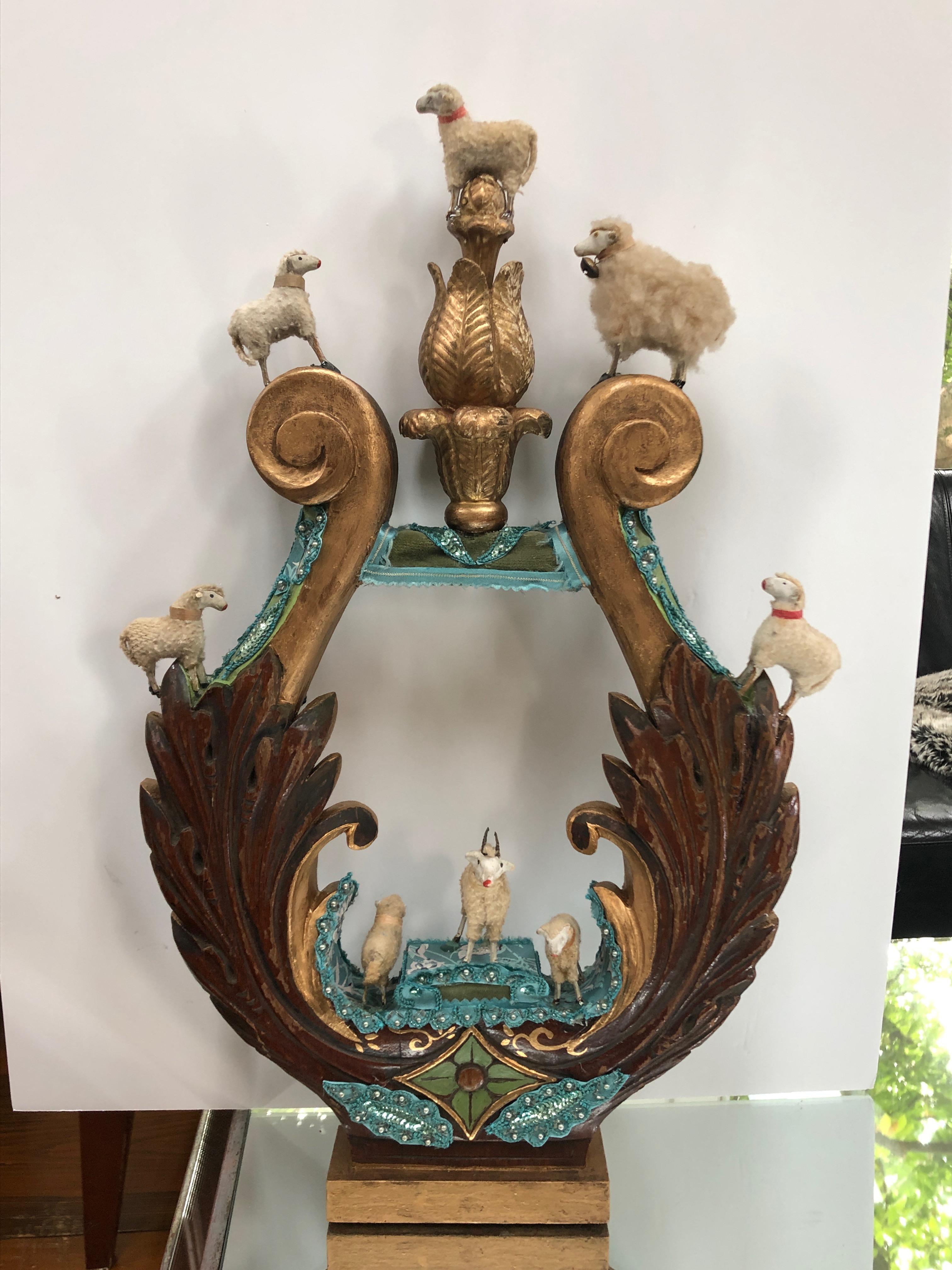 A charming imaginative sculpture created on a vintage carved wood fragment in the shape of a lyre, intricately adorned with European handmade antique lambs, an old finial, a mix of fabrics and hand painted by the renowned Princeton artist, Fay