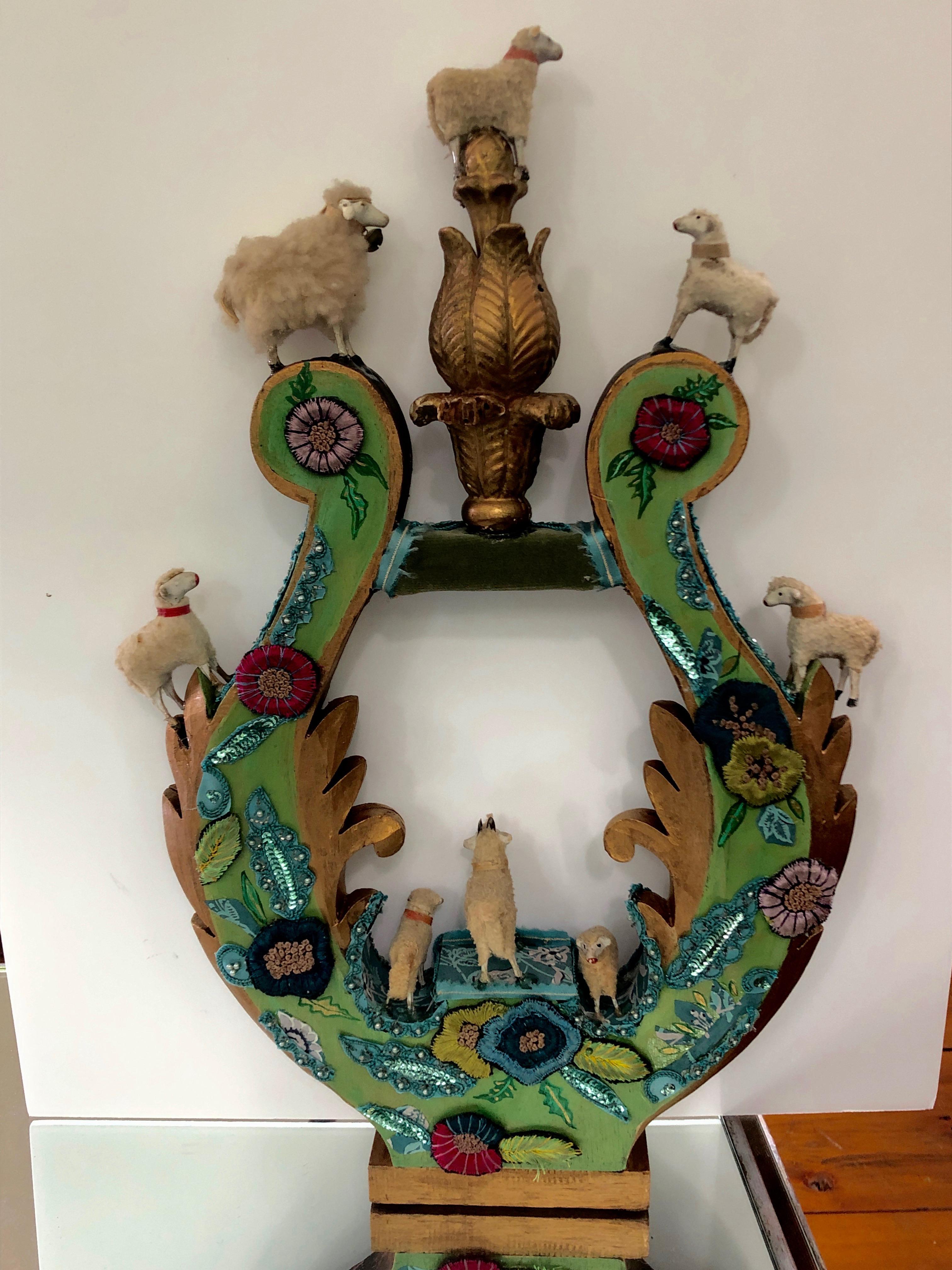 A charming imaginative sculpture created on a vintage carved wood fragment in the shape of a lyre, intricately adorned with European Folk Art handmade antique lambs, an old finial, a mix of fabrics and hand painted by the renowned Princeton artist,
