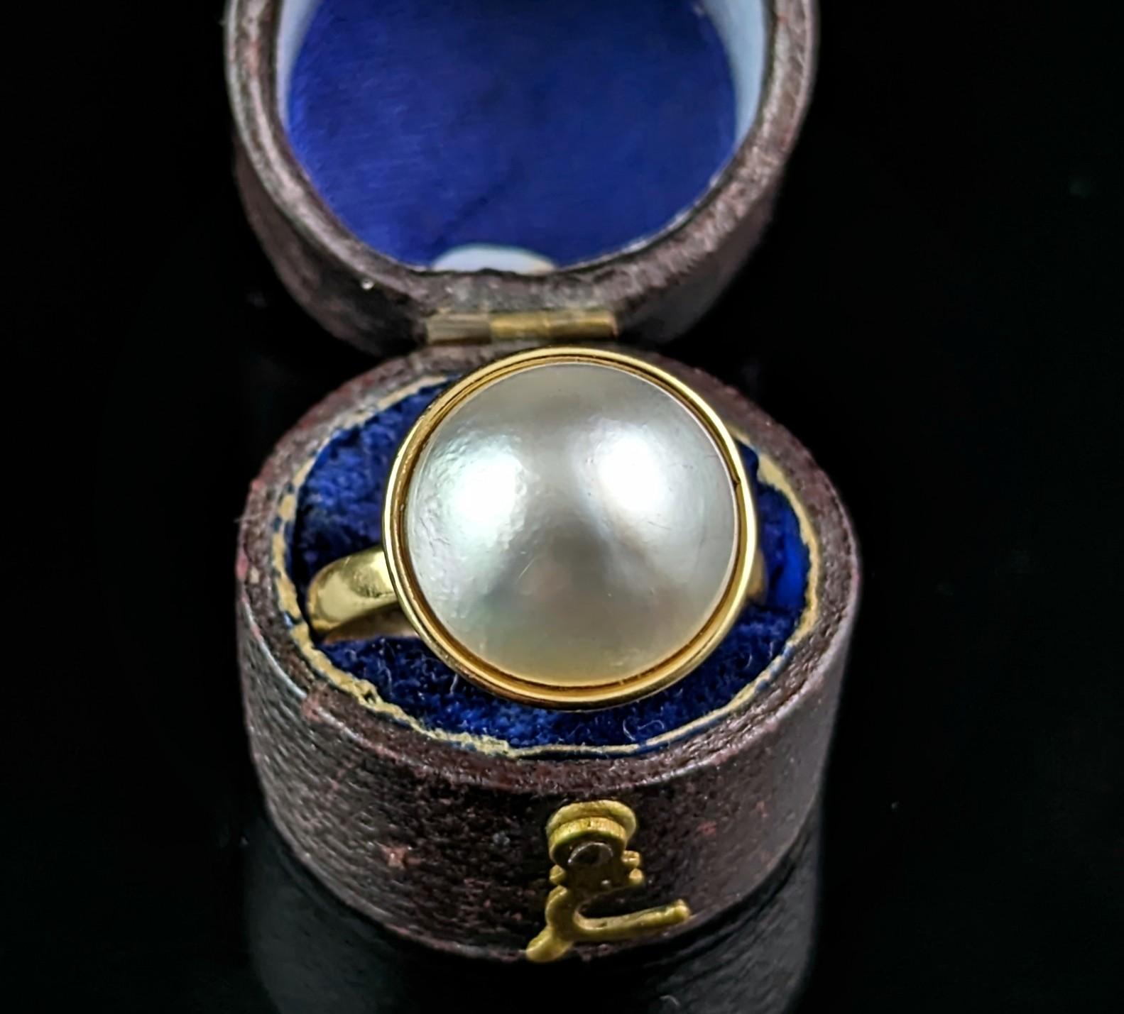 This gorgeous vintage Mabe pearl cocktail ring really makes a statement!

A large lustrous Mabe pearl takes centre stage at the face of the ring, it is in a closed back setting with a rich yellow gold bezel frame.

The band is the same rich 18ct