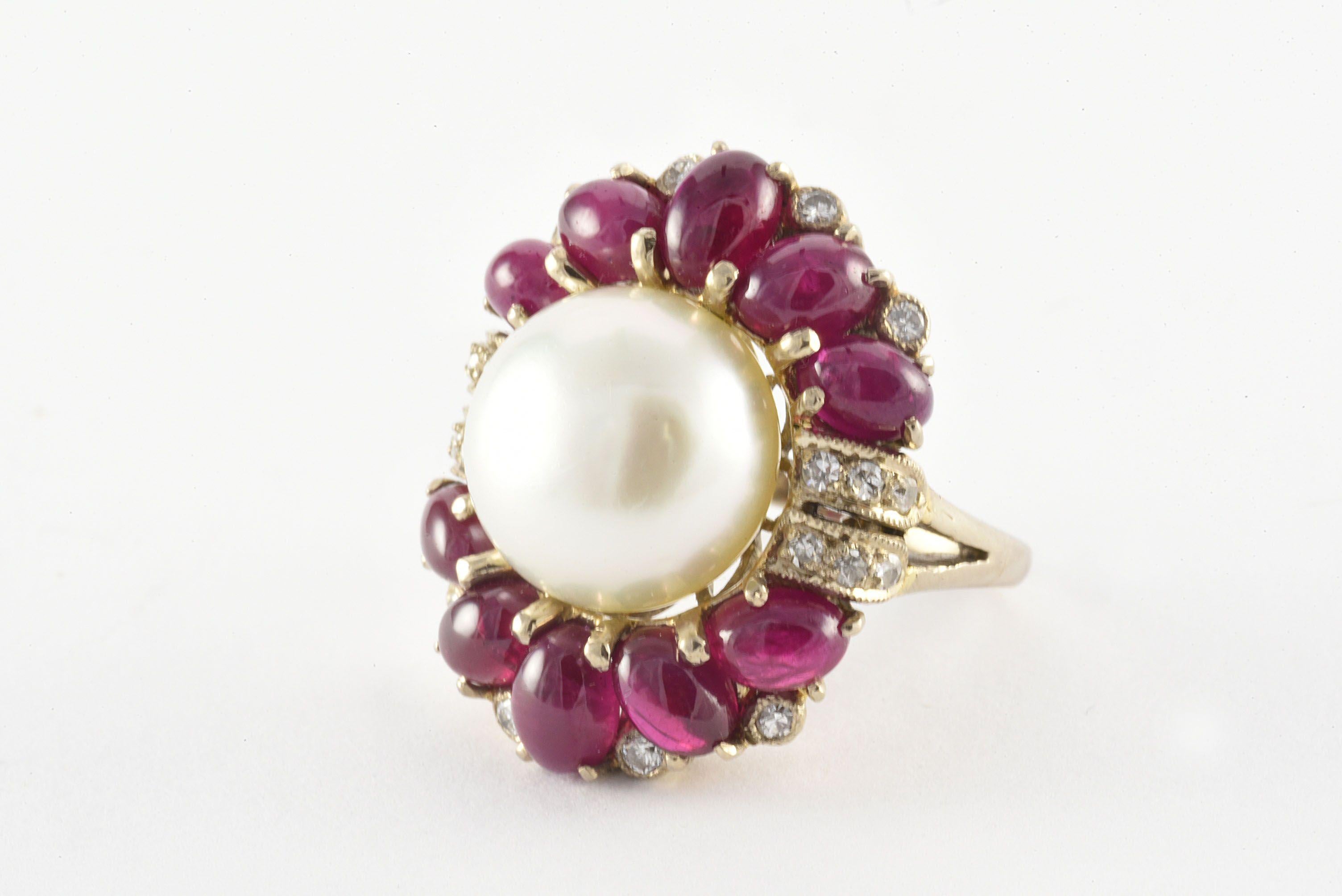 Crafted in the 1940s, this stunning cocktail ring features a 12mm Mabe pearl surrounded by ten natural cabochon oval-shaped rubies and accented with a mix of twenty Old European and single cut diamonds fashioned in 18kt white gold. The diamonds