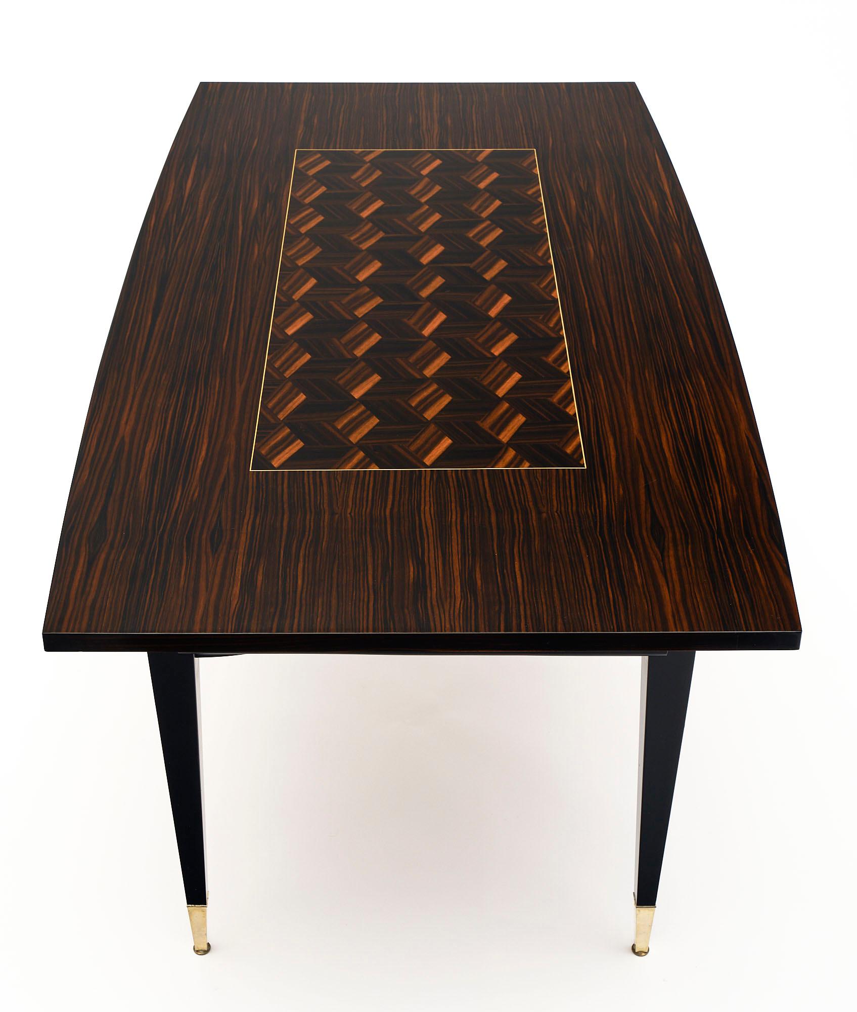 French dining table made of Macassar of ebony wood veneer with a beautiful parquetry design. It is supported by tapered legs capped in brass. Each side has pulls that enable a leaf to be added to extend the surface area. Each adds an additional