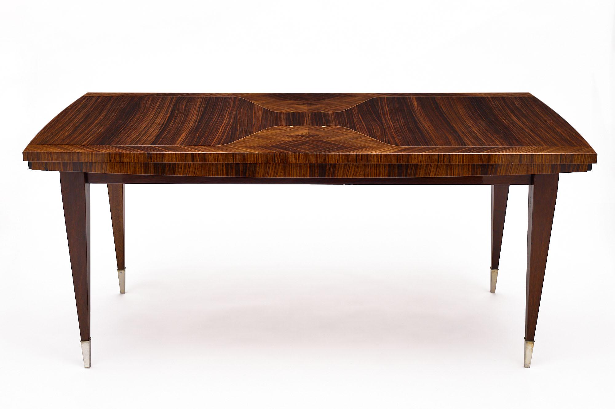 Dining room table from France. This vintage piece in the Modernist style is made of rare Macassar of ebony wood veneer with lemon wood inlays. We love the tapered legs featuring brass feet. There are pulls for leaves; though the leaves are not