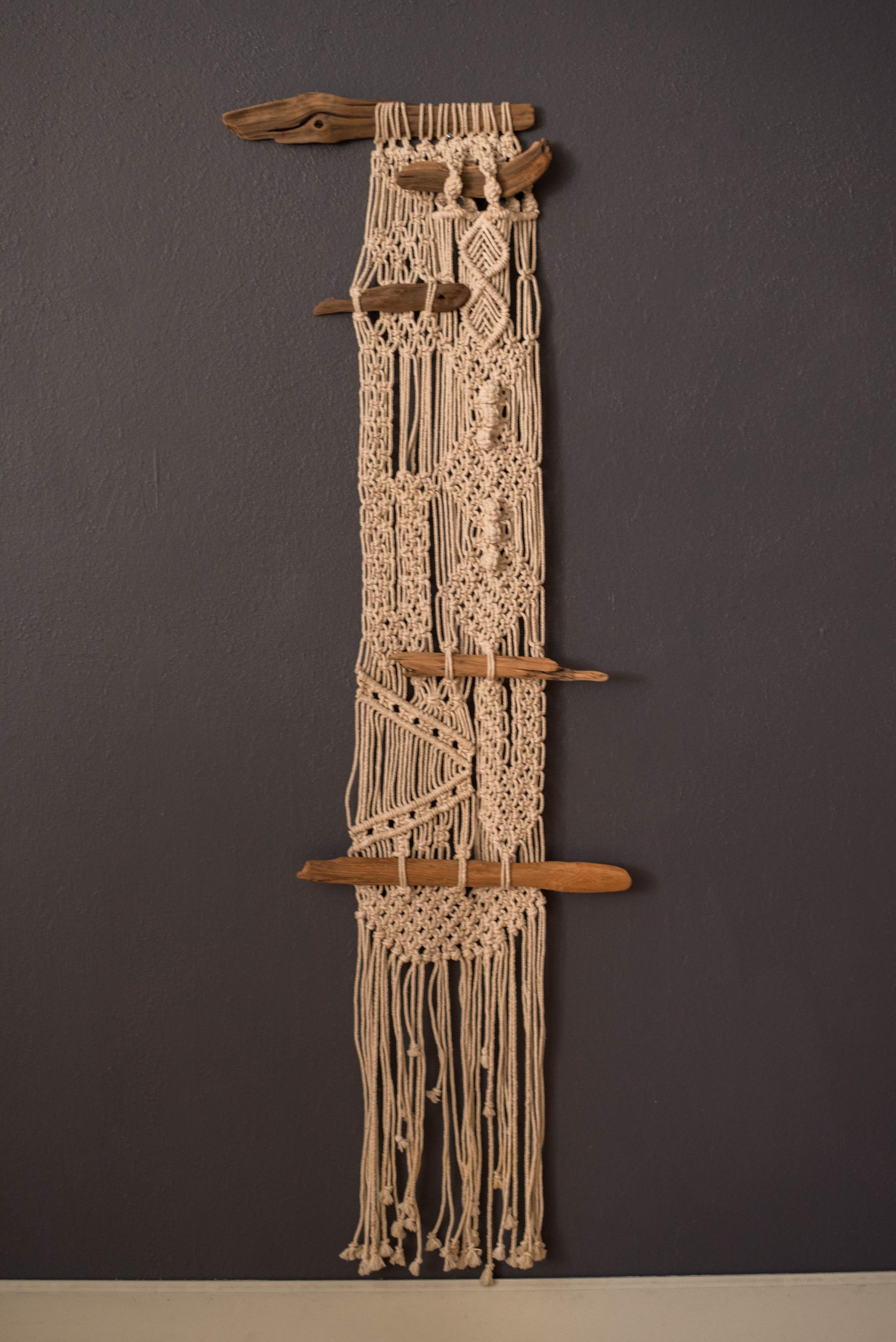 Vintage original macrame fiber art backdrop tapestry, circa 1970s. Features an intricate pattern of hand knotted designs accented with abstract pieces of driftwood. This vertical hanging wall piece adds natural texture and Dimension to any Bohemian