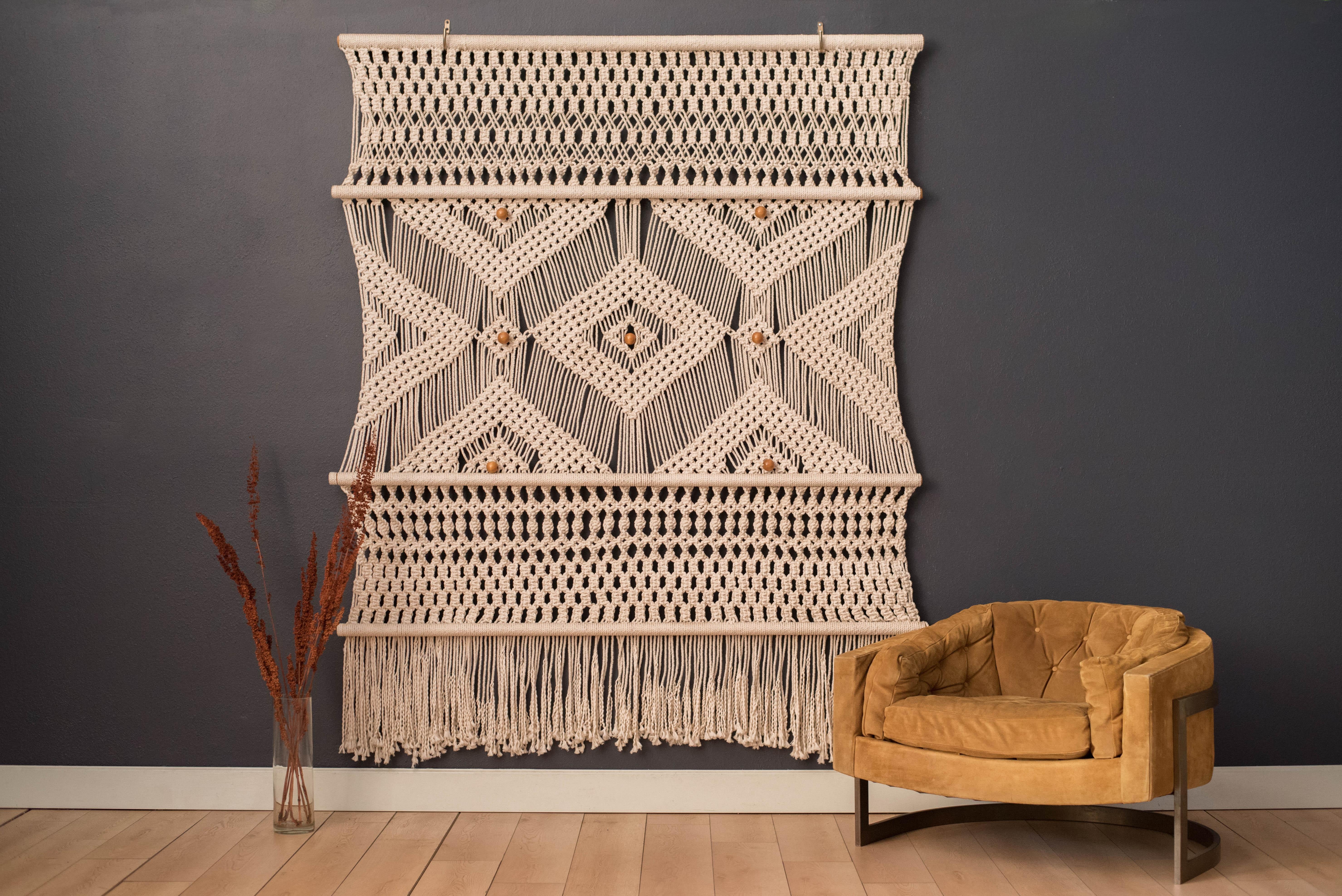 Vintage original fiber art backdrop tapestry, circa 1970s. This oversized piece features a geometric pattern of hand knotted designs accented with wood macrame beads. Adds a natural texture and dimension to any Bohemian or Mid-Century Modern space.