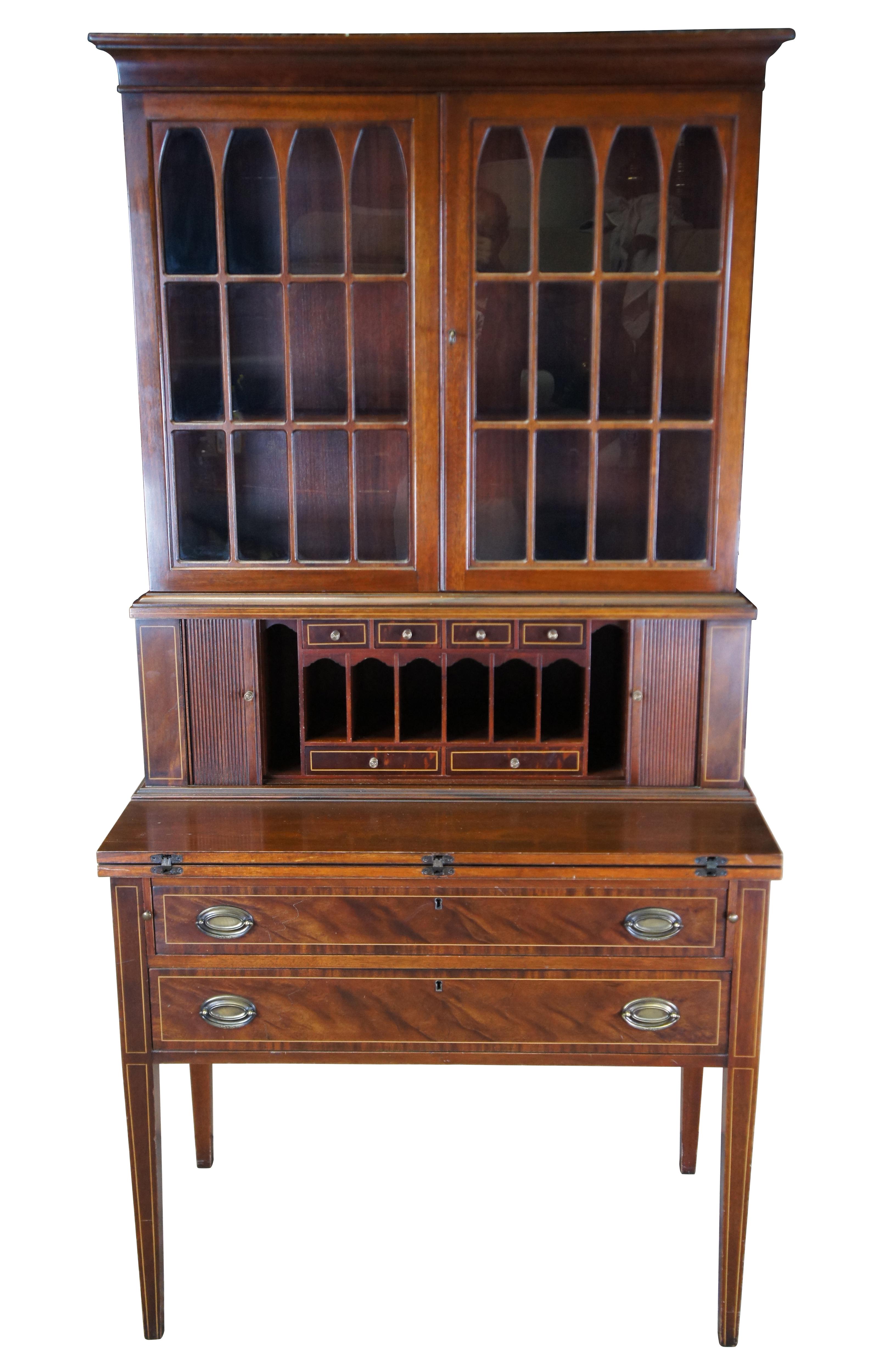 An exceptional vintage Hepplewhite-style secretary by Maddox, circa 1930s. This beautiful specimen is made from mahogany with an upper bookcase having double mullioned glass doors over a central compartment with tambour doors.  The doors open to