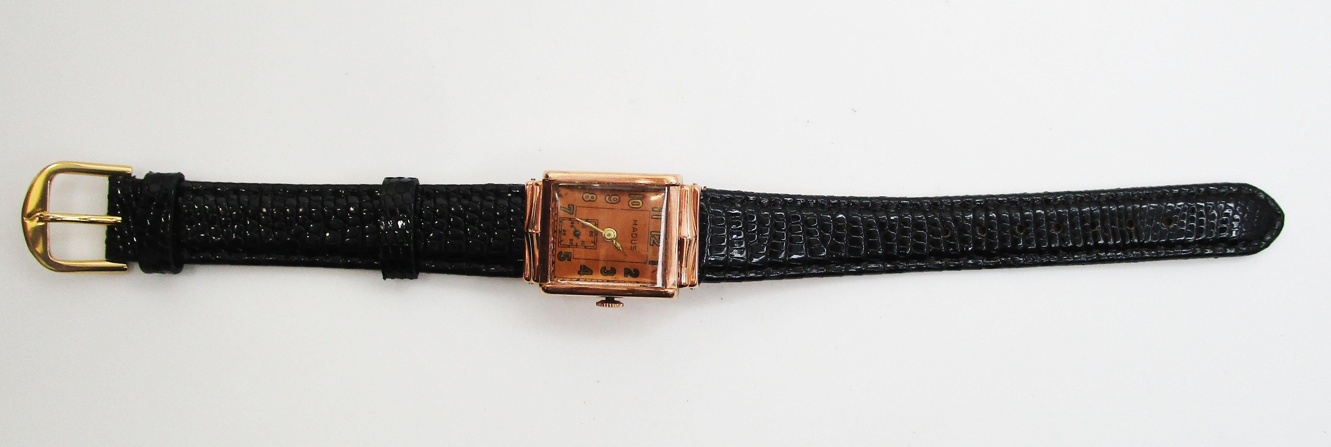 This incredible vintage watch is a 14k rose gold Madus watch with a genuine lizard strap. The watch has a geometric shape. The face is in rose gold to match the 14k rose gold face, creating a bright and bold final look with a definitive rose gold