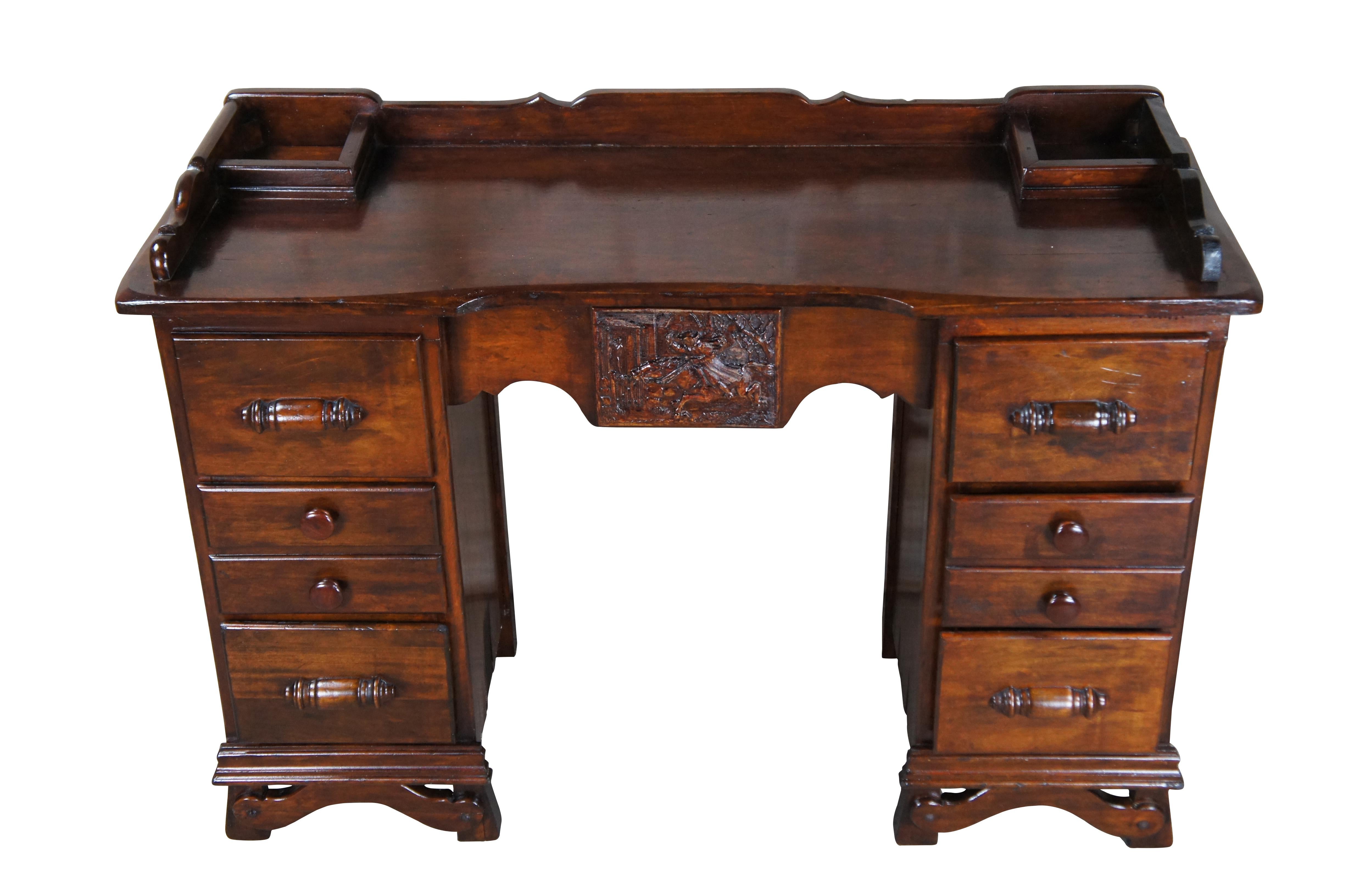Vintage kneehole library / vanity / writing desk.  Made of mahogany featuring traditional styling with upper gallery encasing two cubbies or ink compartments over multiple drawers and carved colonial scene with man on horseback riding past a