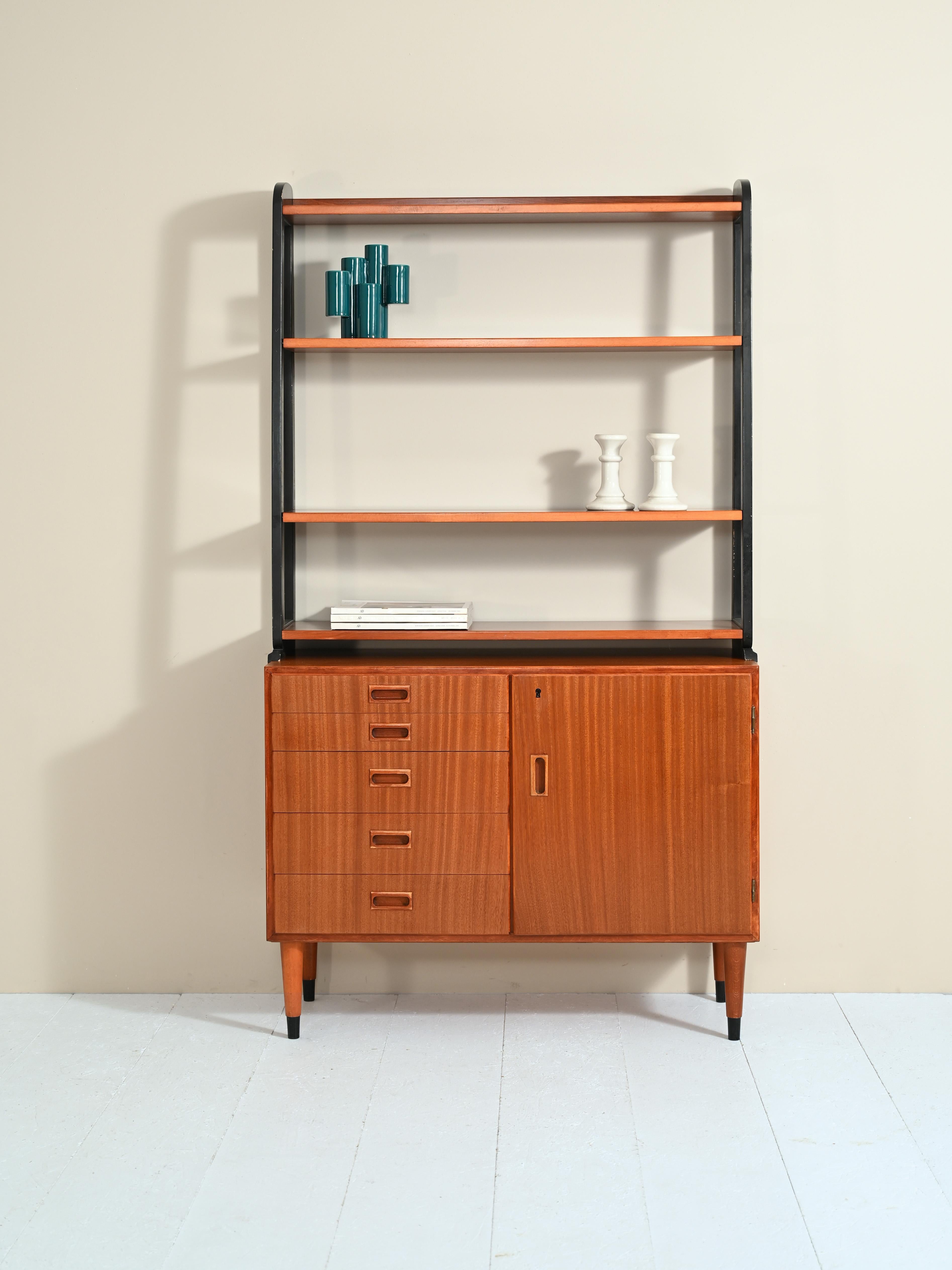 Scandinavian-made bookcase produced in the 1950s.

The cabinet consists of two parts: the lower part consists of five drawers and a door concealing a shelving unit.

The upper part consists of four shelves with the side supports painted