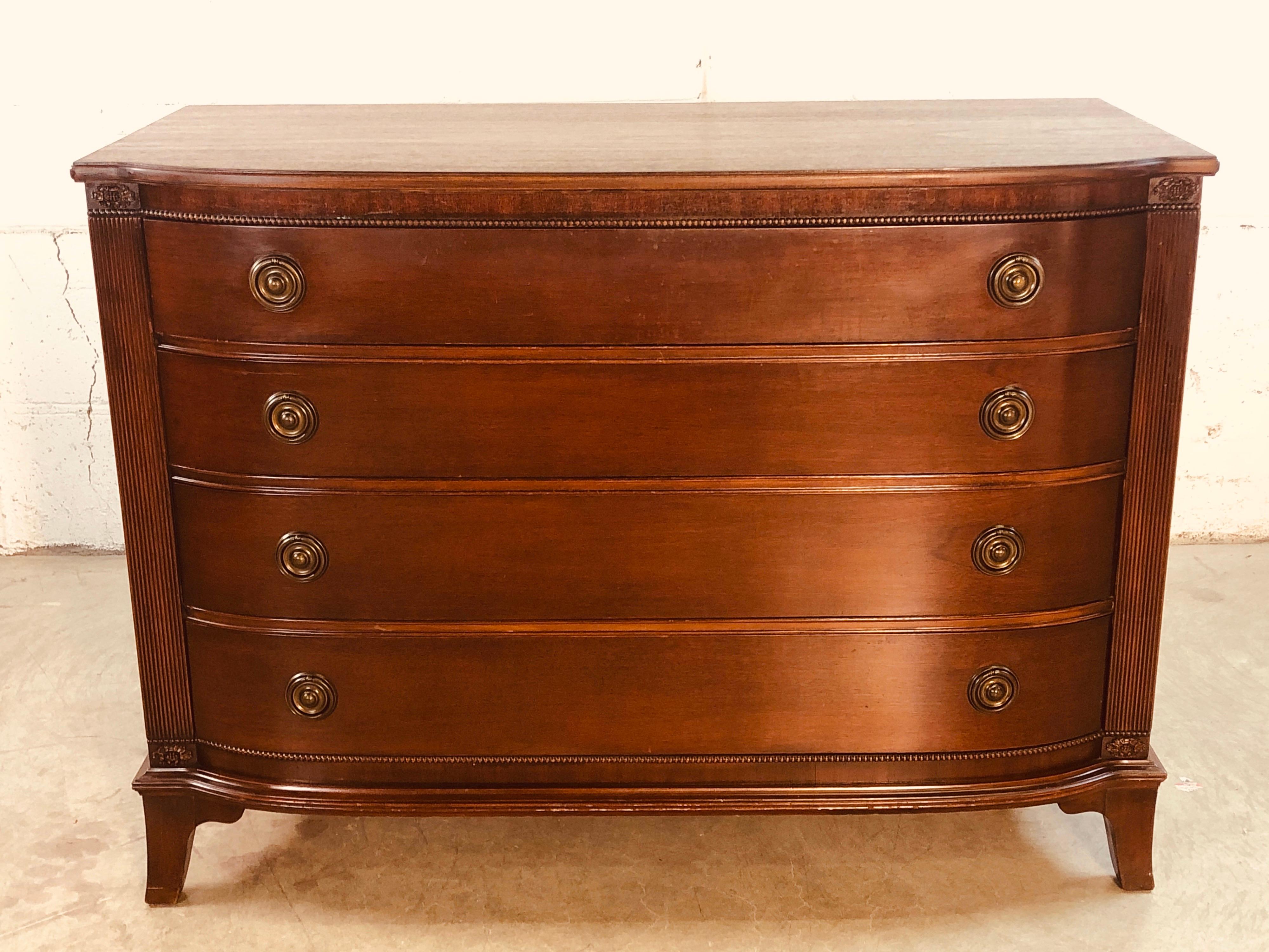 Vintage 1950s curved front mahogany dresser with four drawers and round brass pulls. The dresser has federal style columns on each side and floral carved accents. Original condition with light wear from use. No marks.